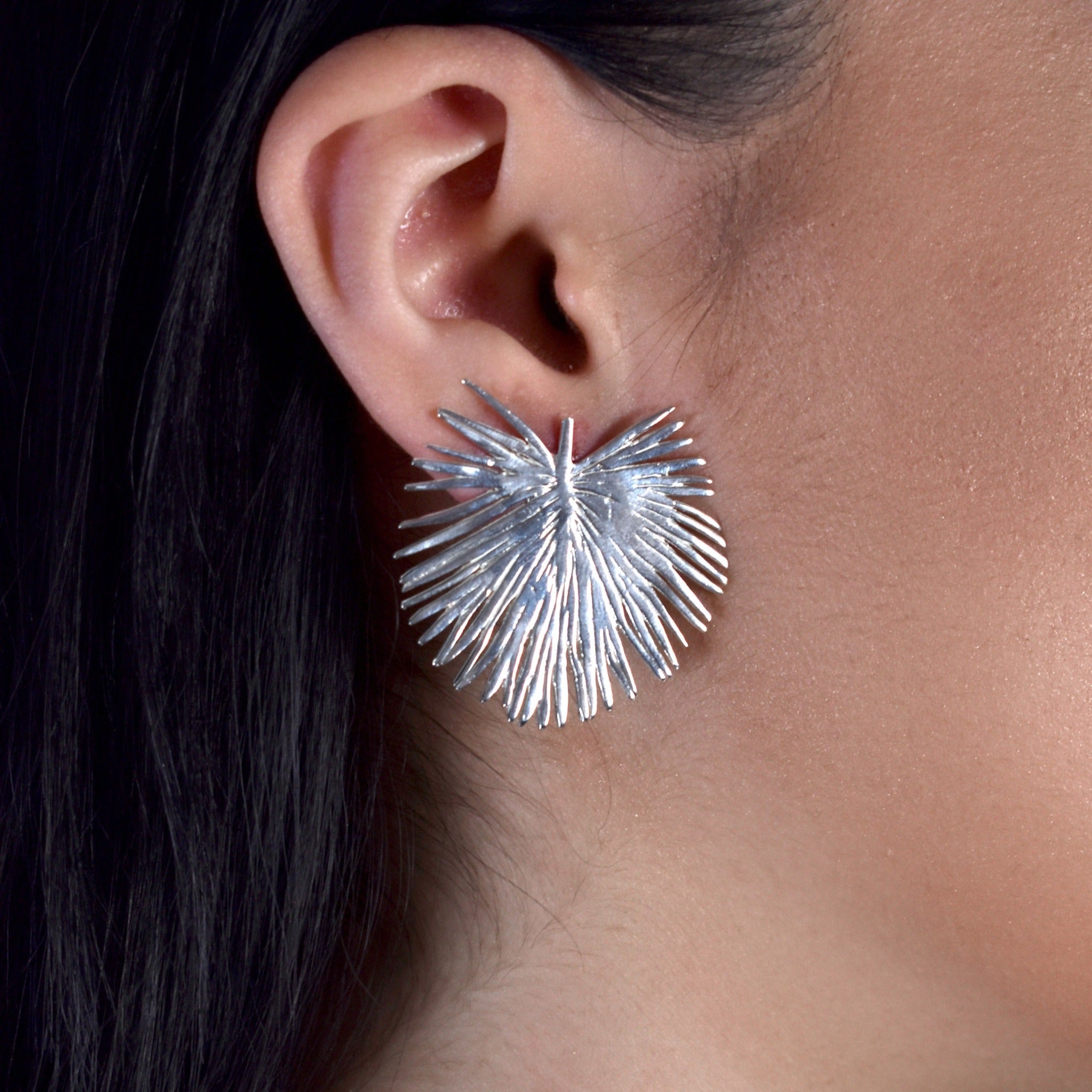 Solid sterling silver stud earrings made by hand shaped like a palm leaf on model