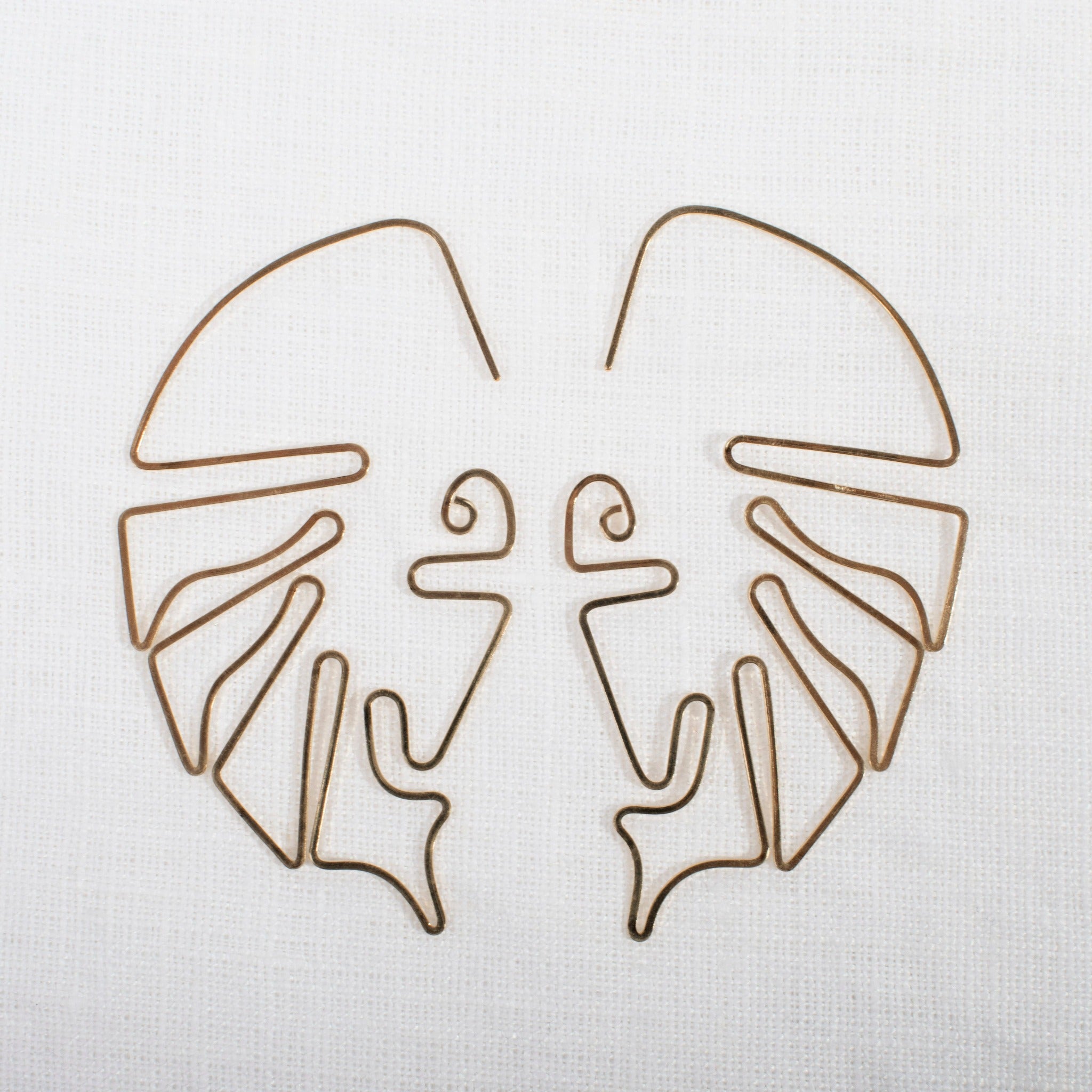 monstera shaped gold earrings on white fabric background