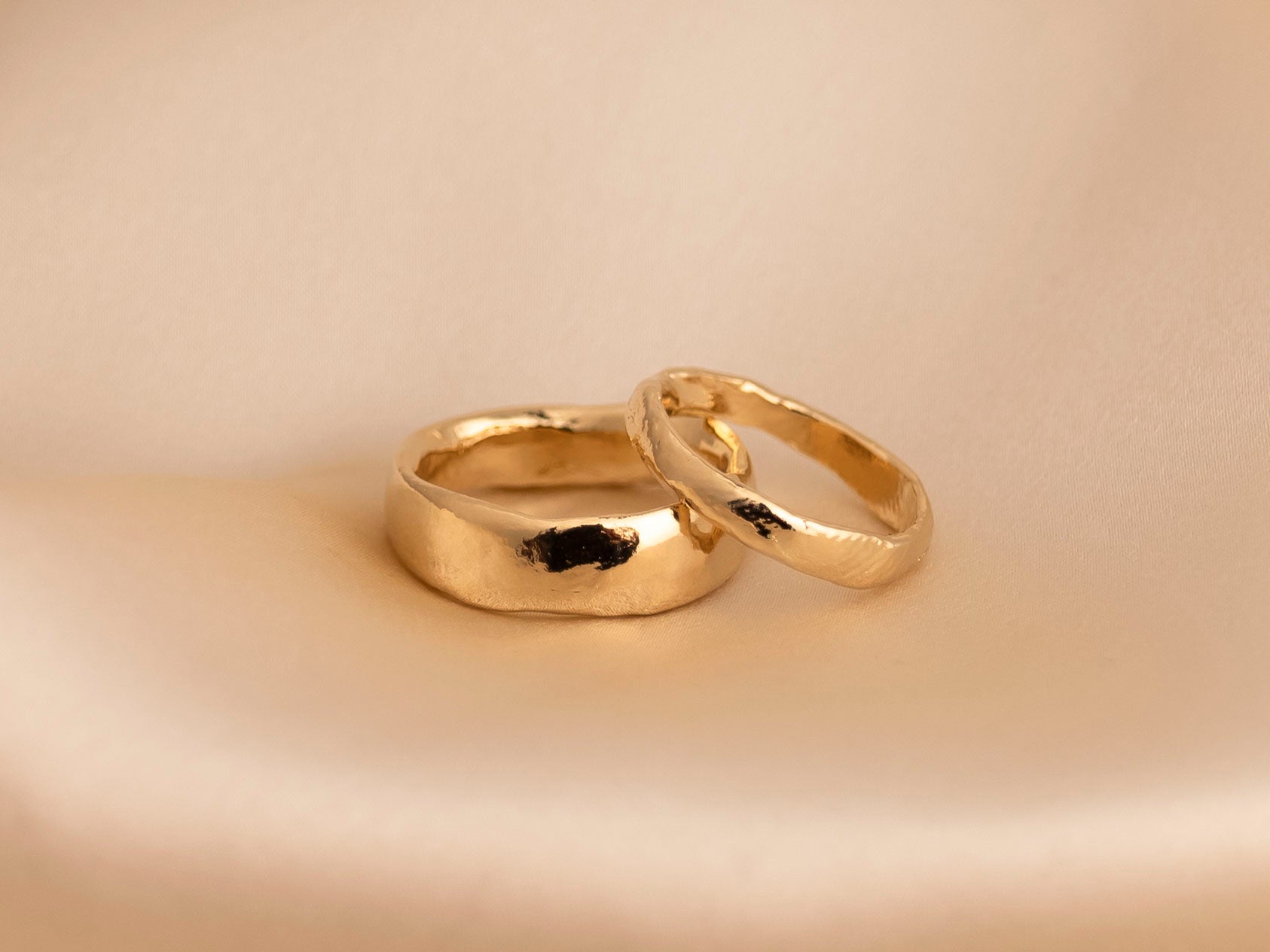 Pair of hand-carved yellow gold wedding bands on a beige background