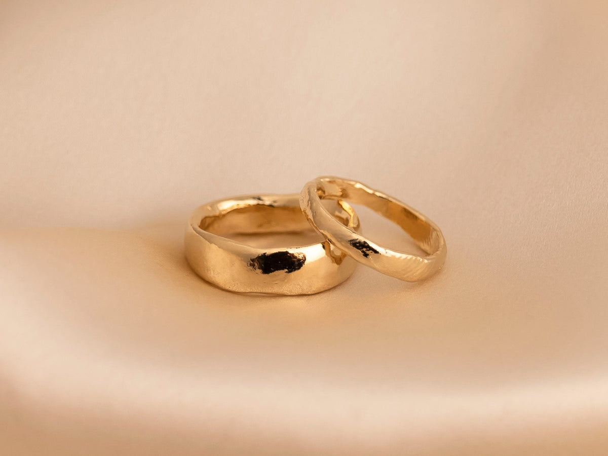 Pair of hand-carved yellow gold wedding bands on a beige background