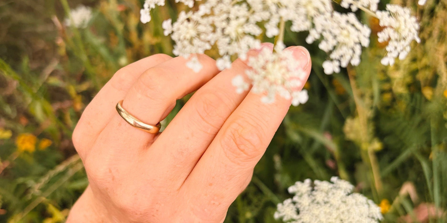 Thin yellow gold wedding band worn on a hand beside white flowers