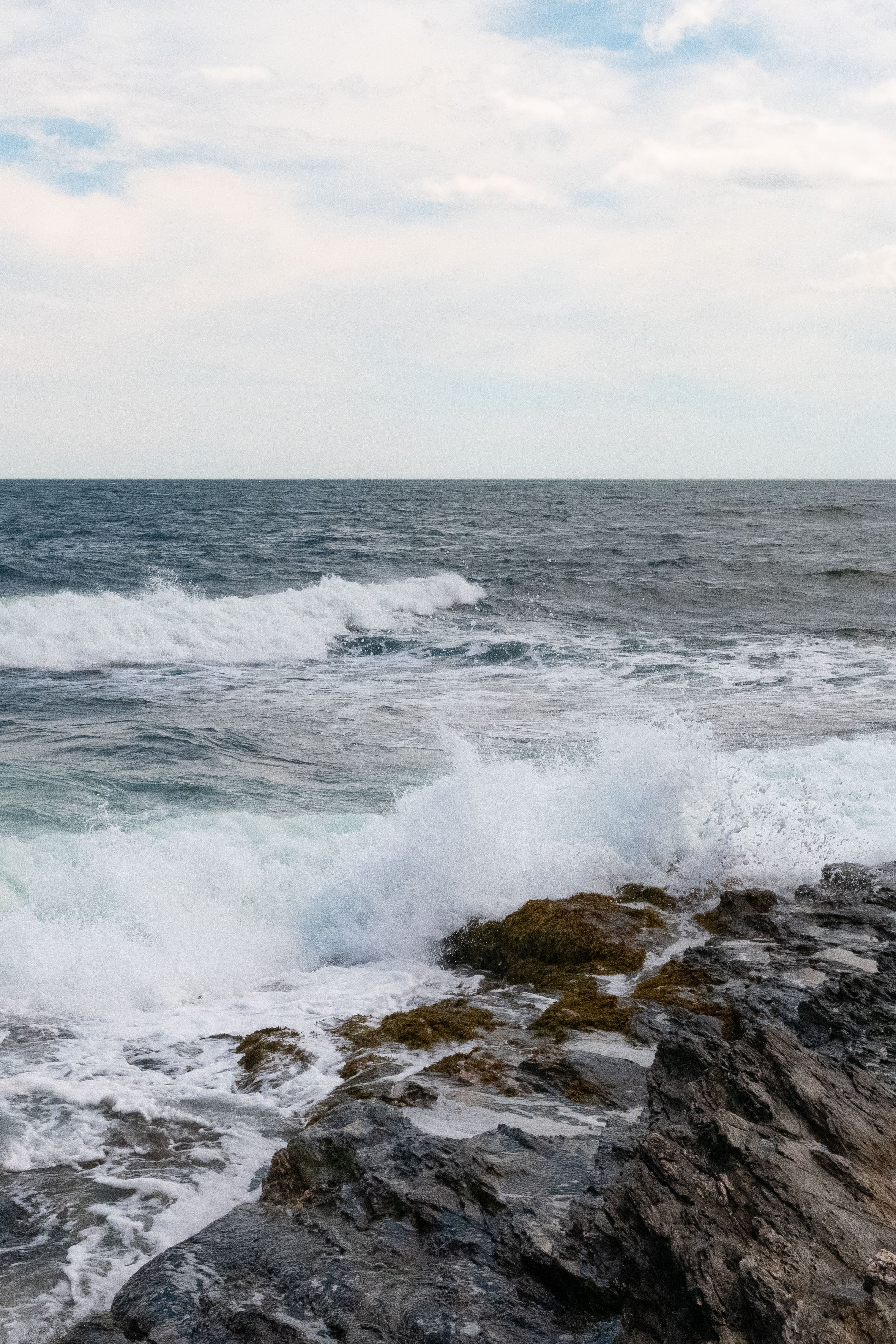 Ocean waves crashing against rocks with a cloudy sky.