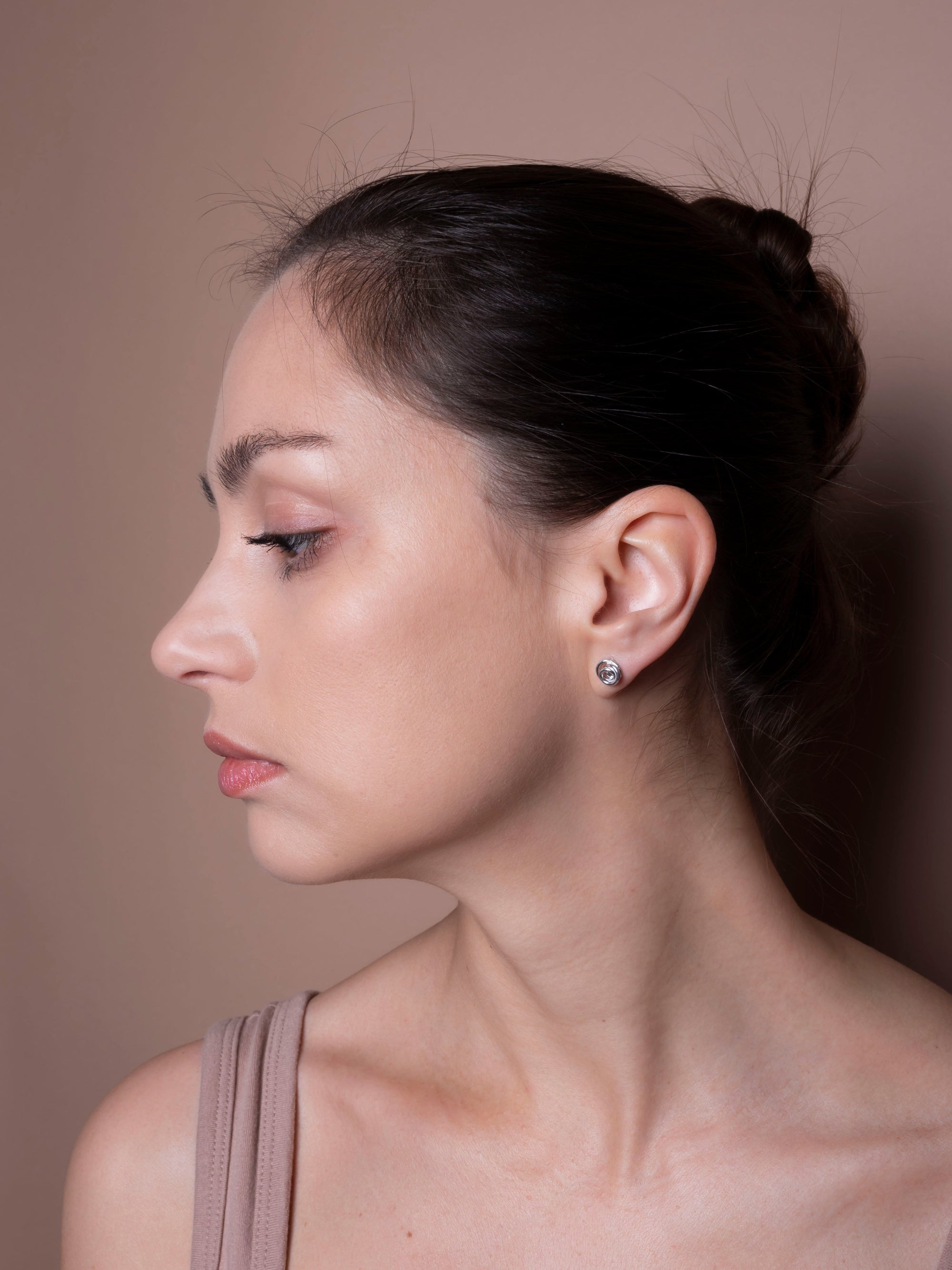 Woman with a bun hairstyle wearing earrings against a neutral background