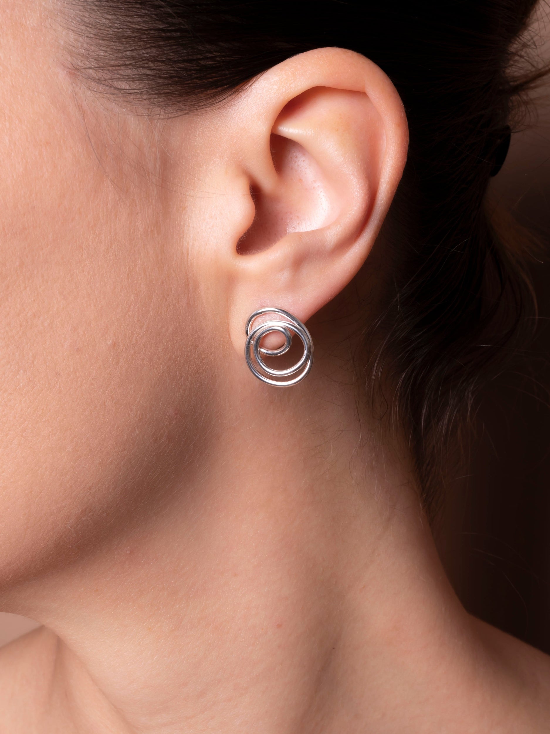 Close-up of an ear wearing a silver earring with two interlocking rings.