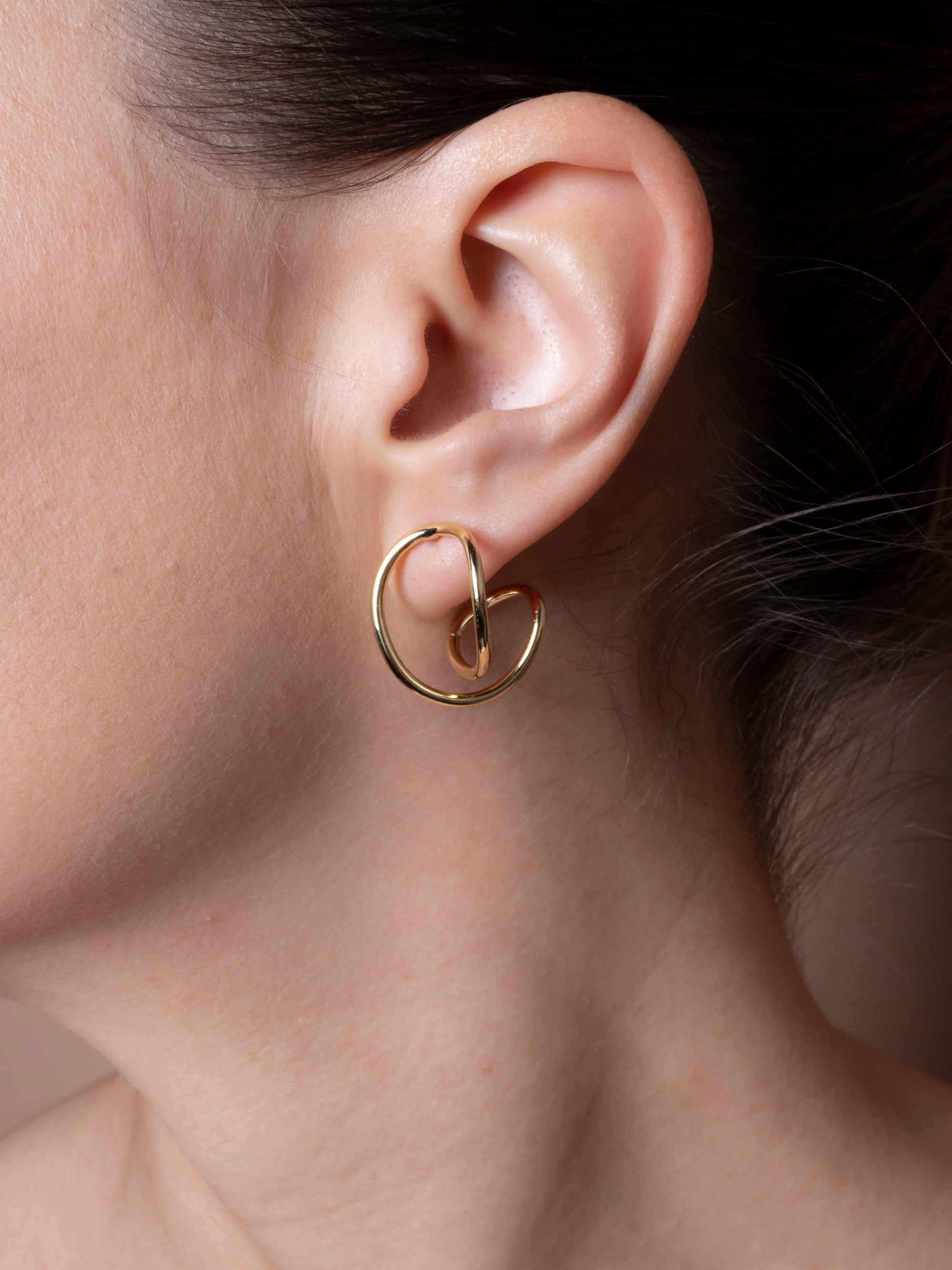 Close-up of an ear wearing a gold hoop earring with a blurred background