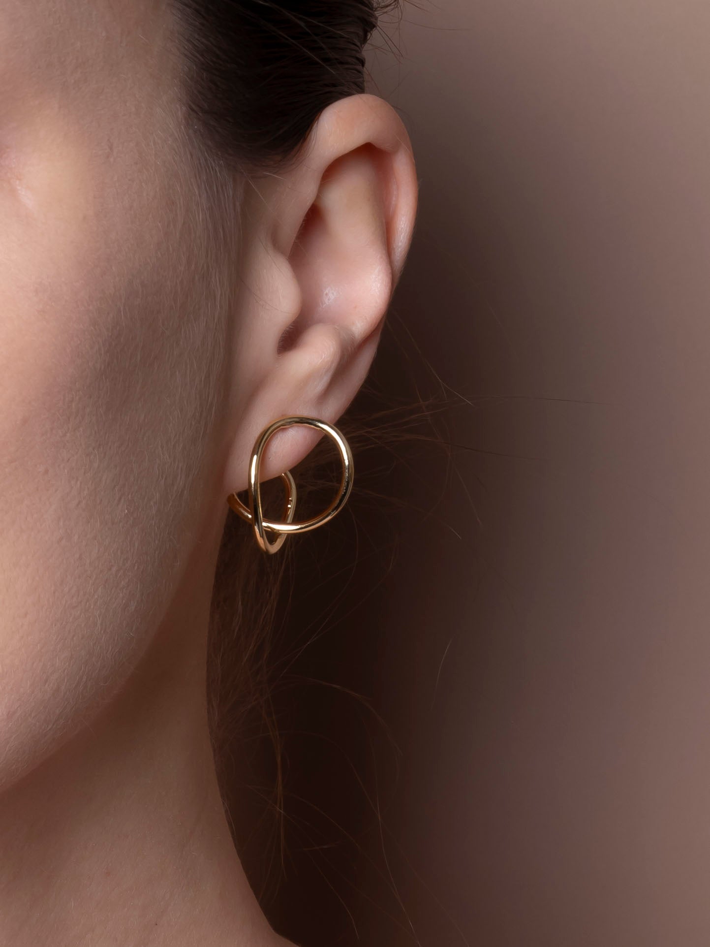 Gold earring worn on an ear with a plain background