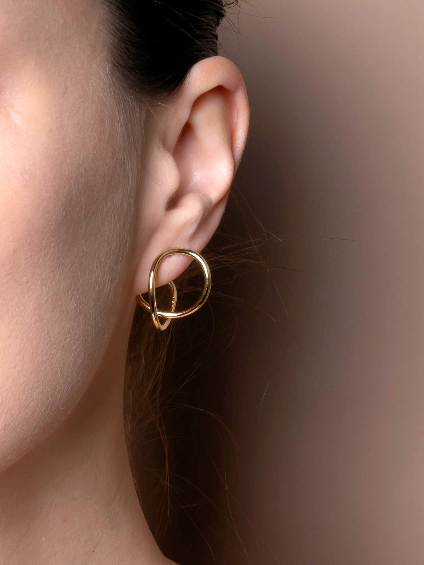 Gold earring worn on an ear with a neutral background