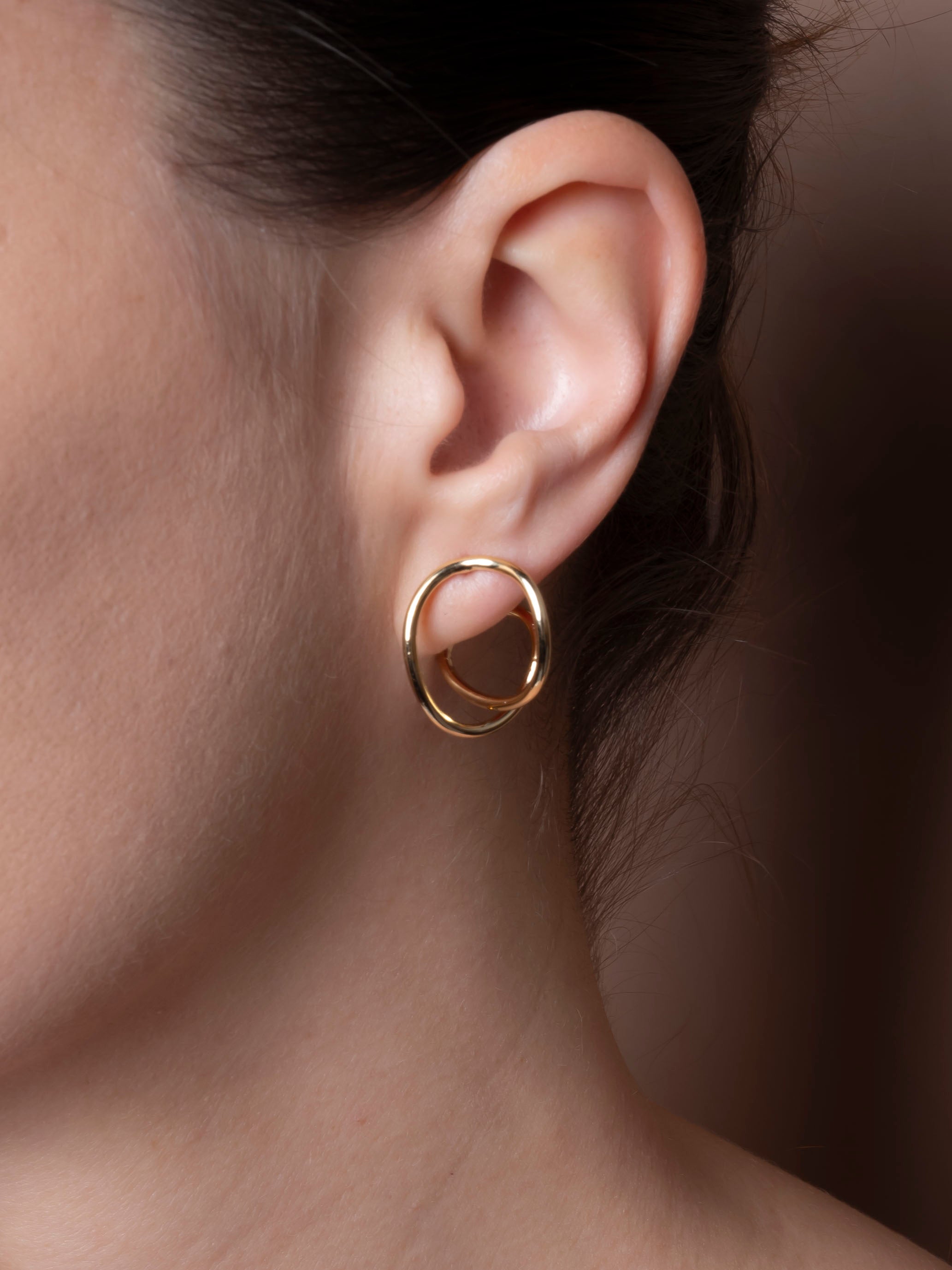 Close-up of an ear wearing a gold hoop earring with a blurred background