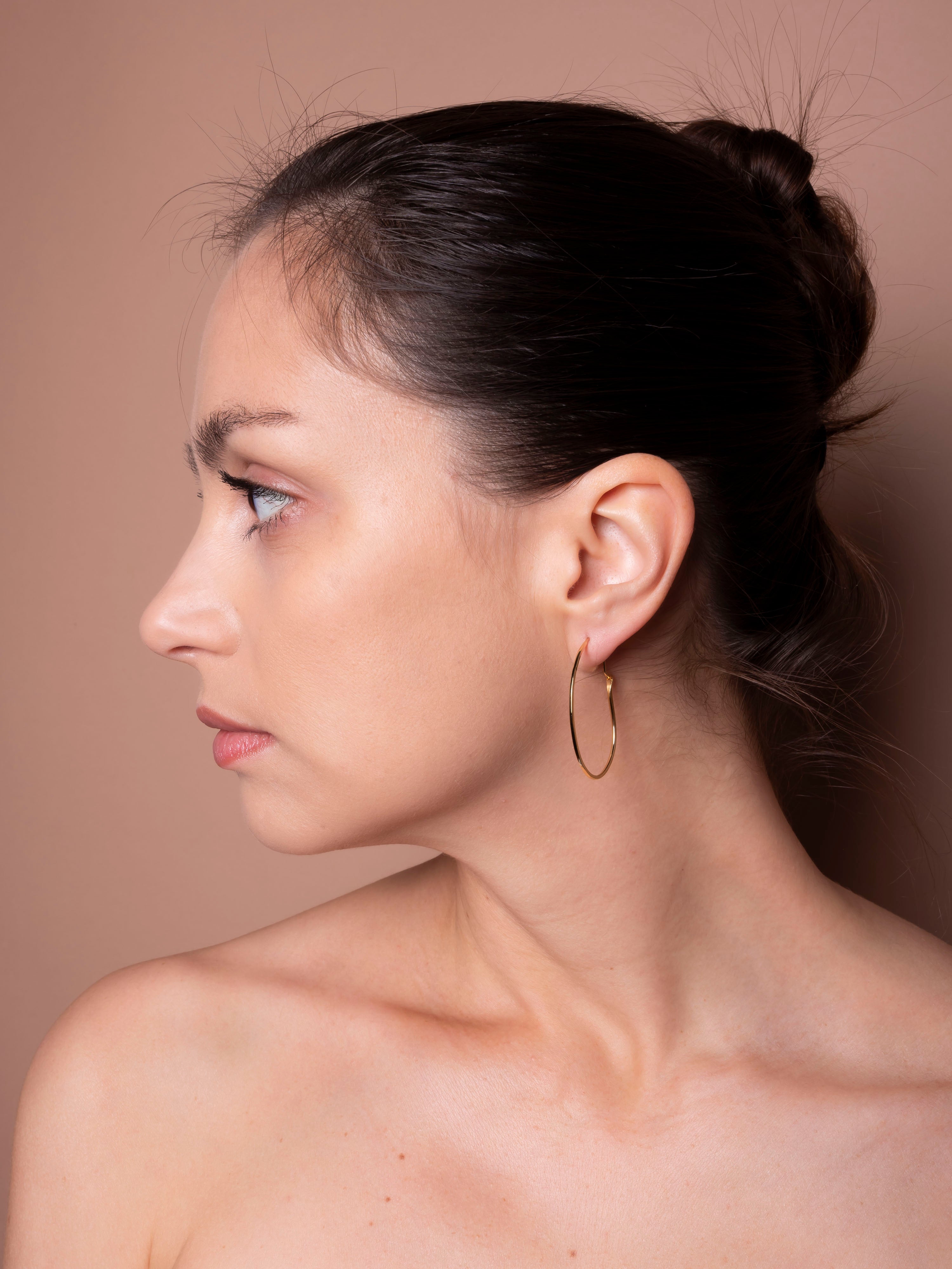 Woman with a side bun wearing gold hoop earrings against a neutral background
