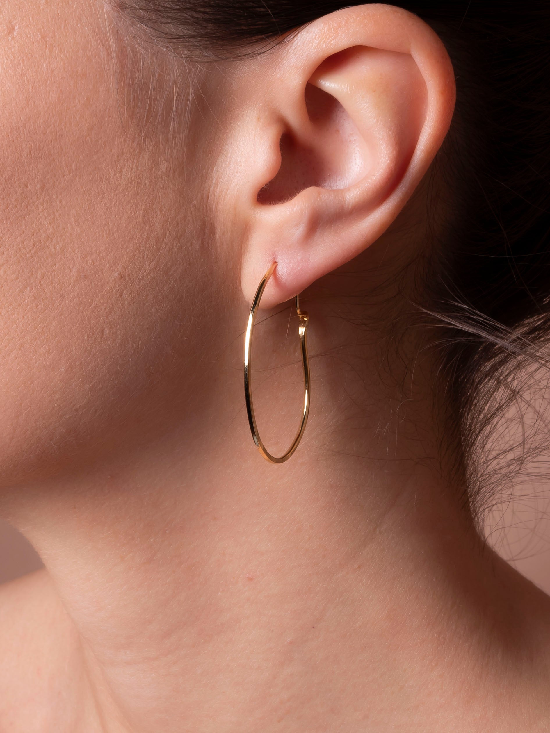 Gold hoop earrings worn by a person with a neutral background
