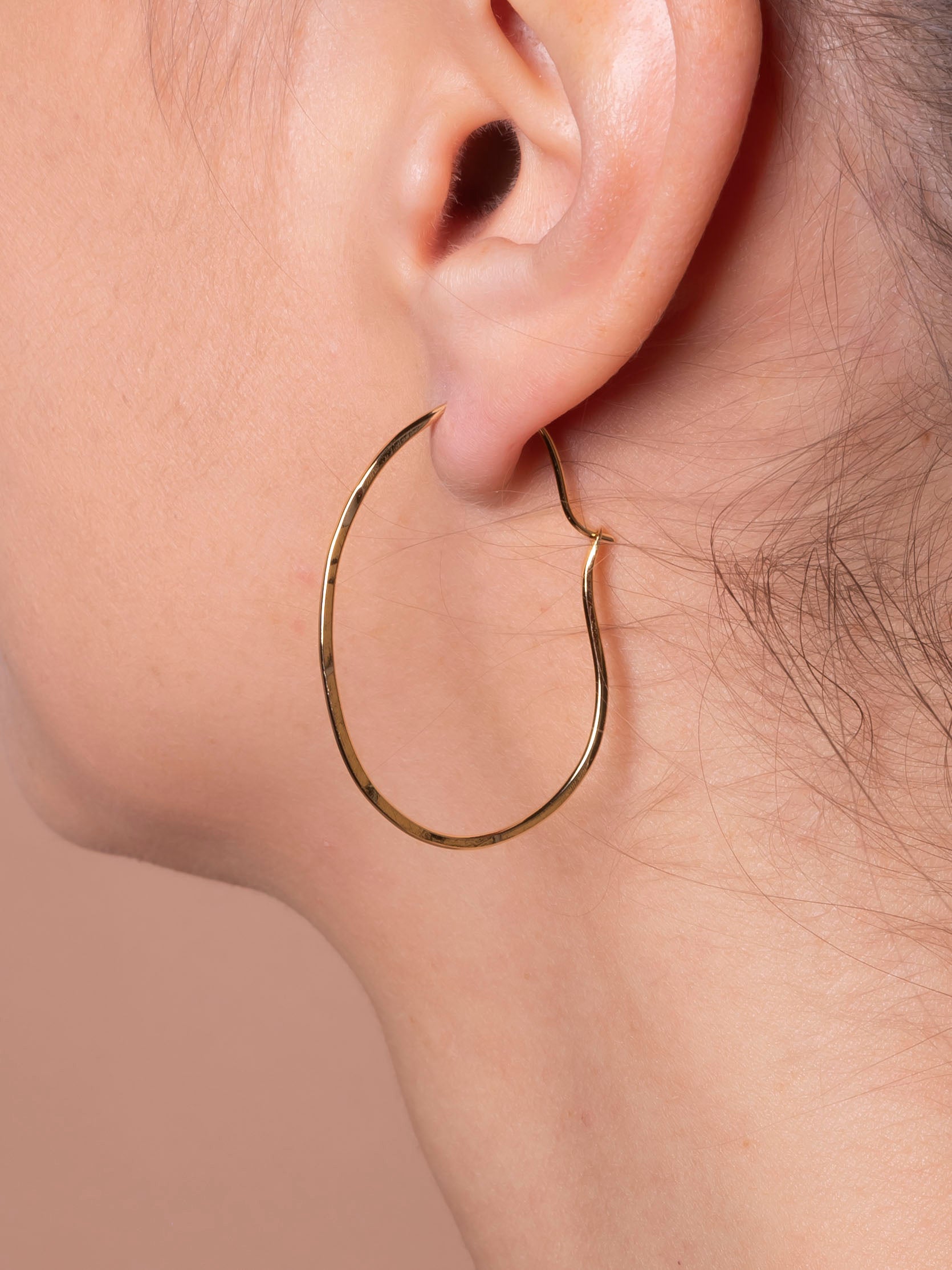 Gold hoop earring worn on a person's ear against a neutral background