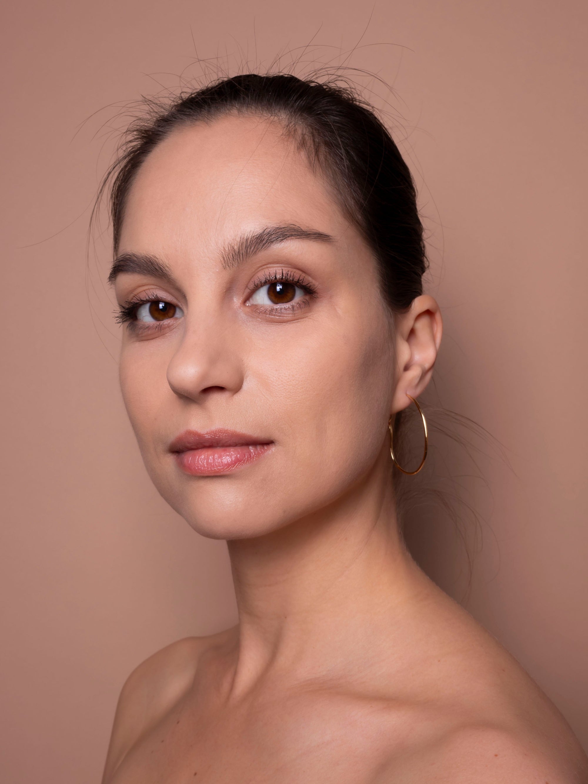 Woman with hoop earrings against a beige background