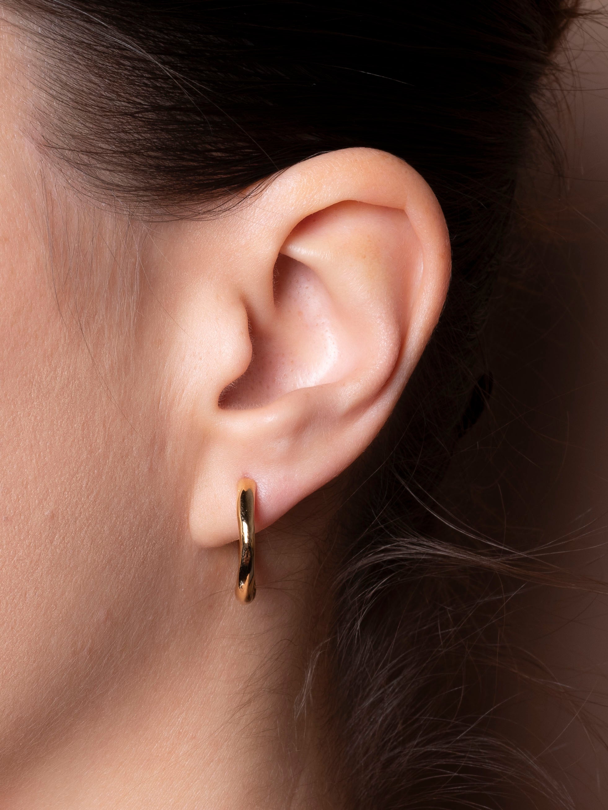 Close-up of an ear wearing a gold hoop earring with a blurred background