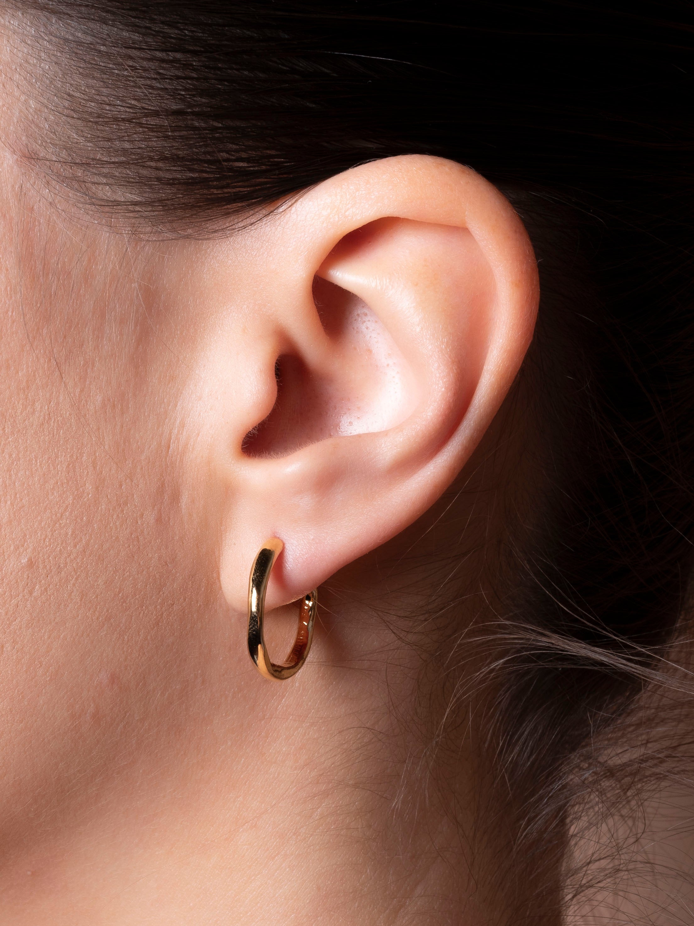 Close-up of an ear wearing a gold hoop earring with a dark background