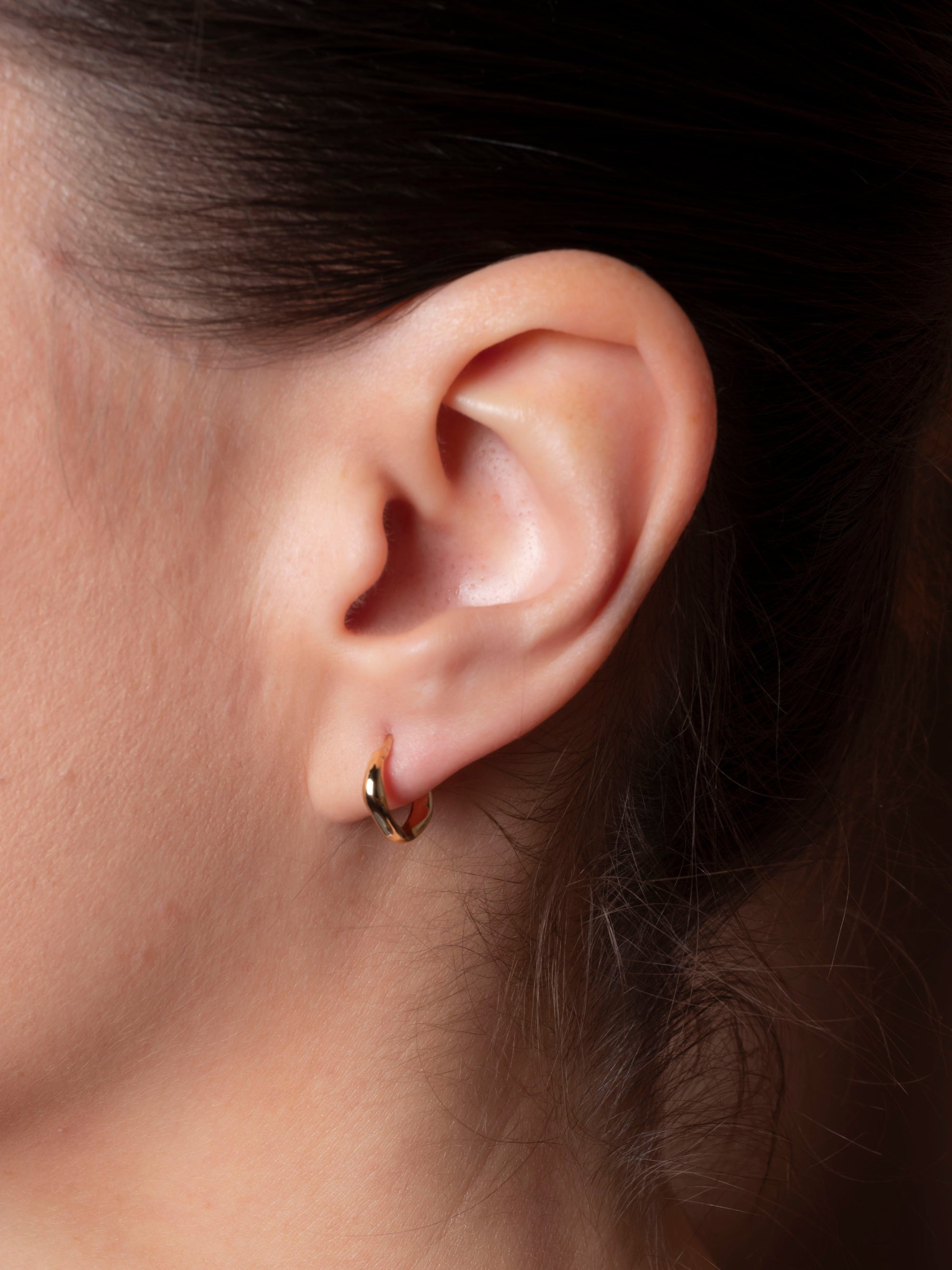 Close-up of an ear wearing a gold hoop earring with a dark background