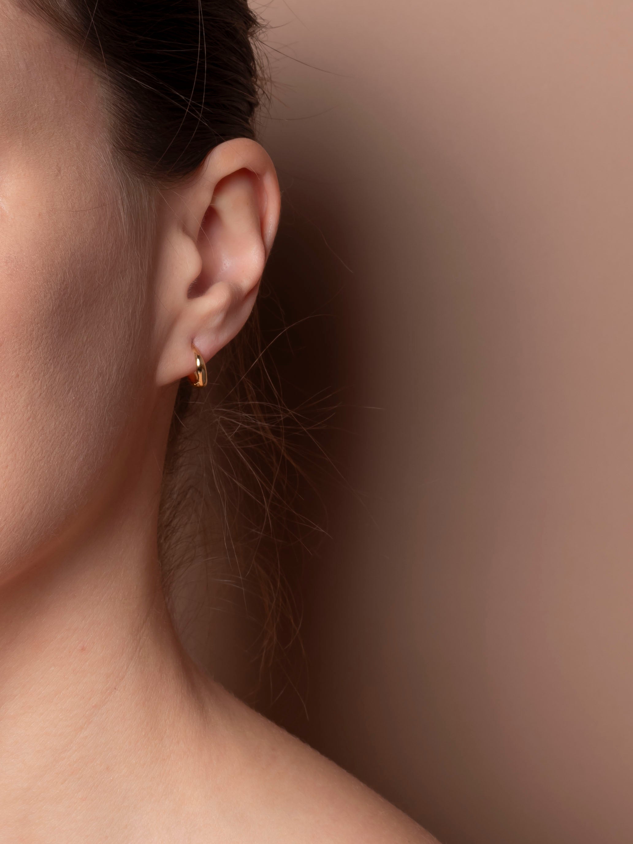Close-up of an ear wearing a gold earring against a neutral background