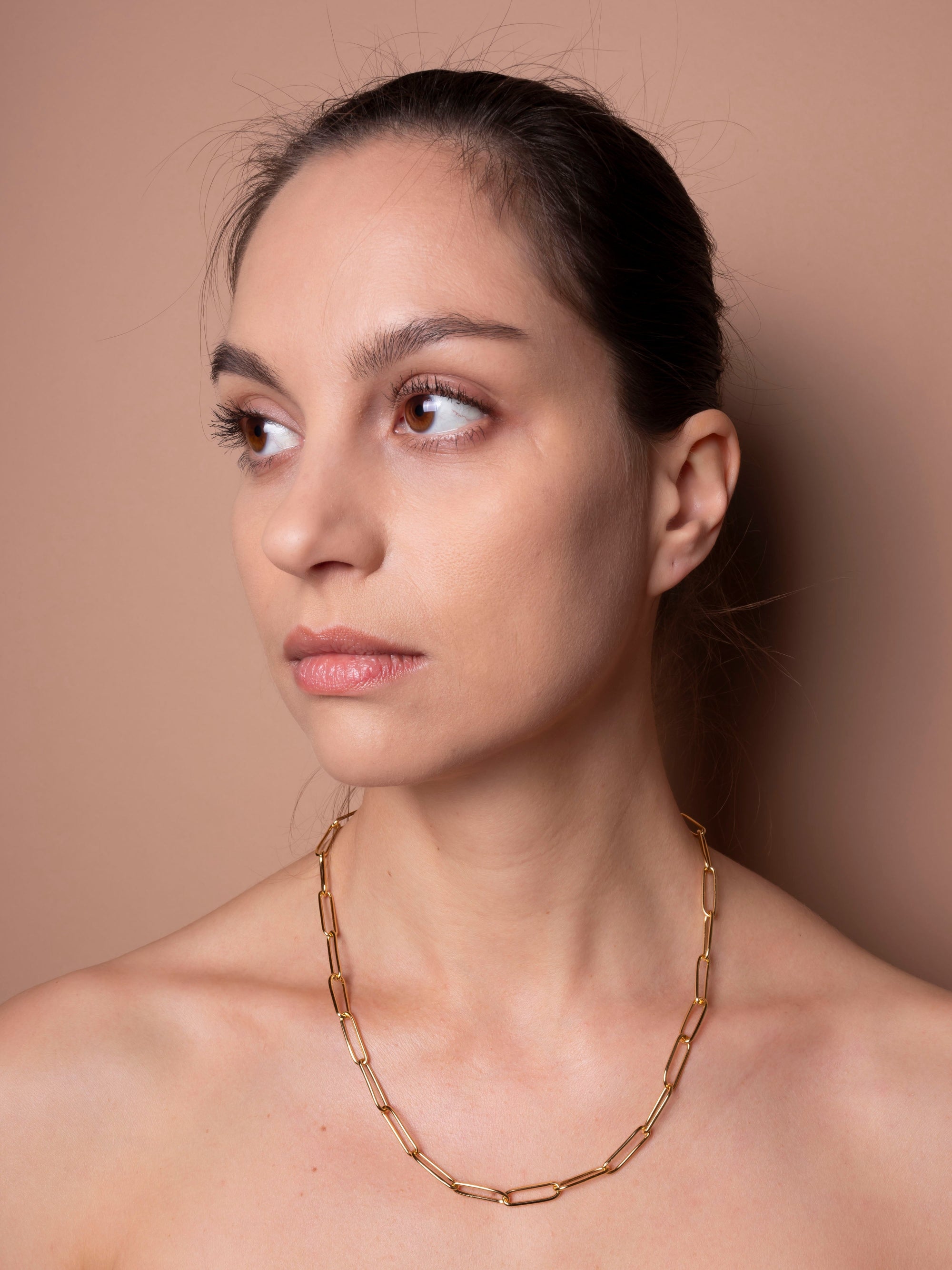 Woman wearing a gold chain necklace against a beige background