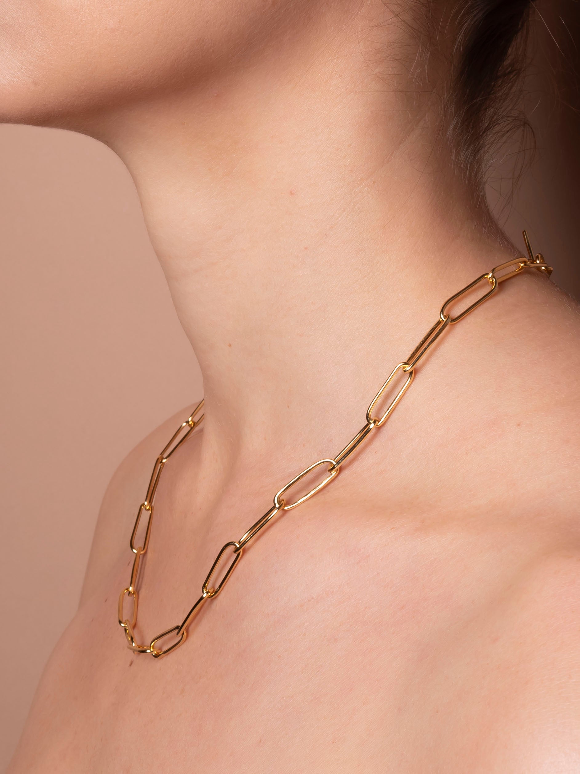 Gold chain necklace on a person against a neutral background