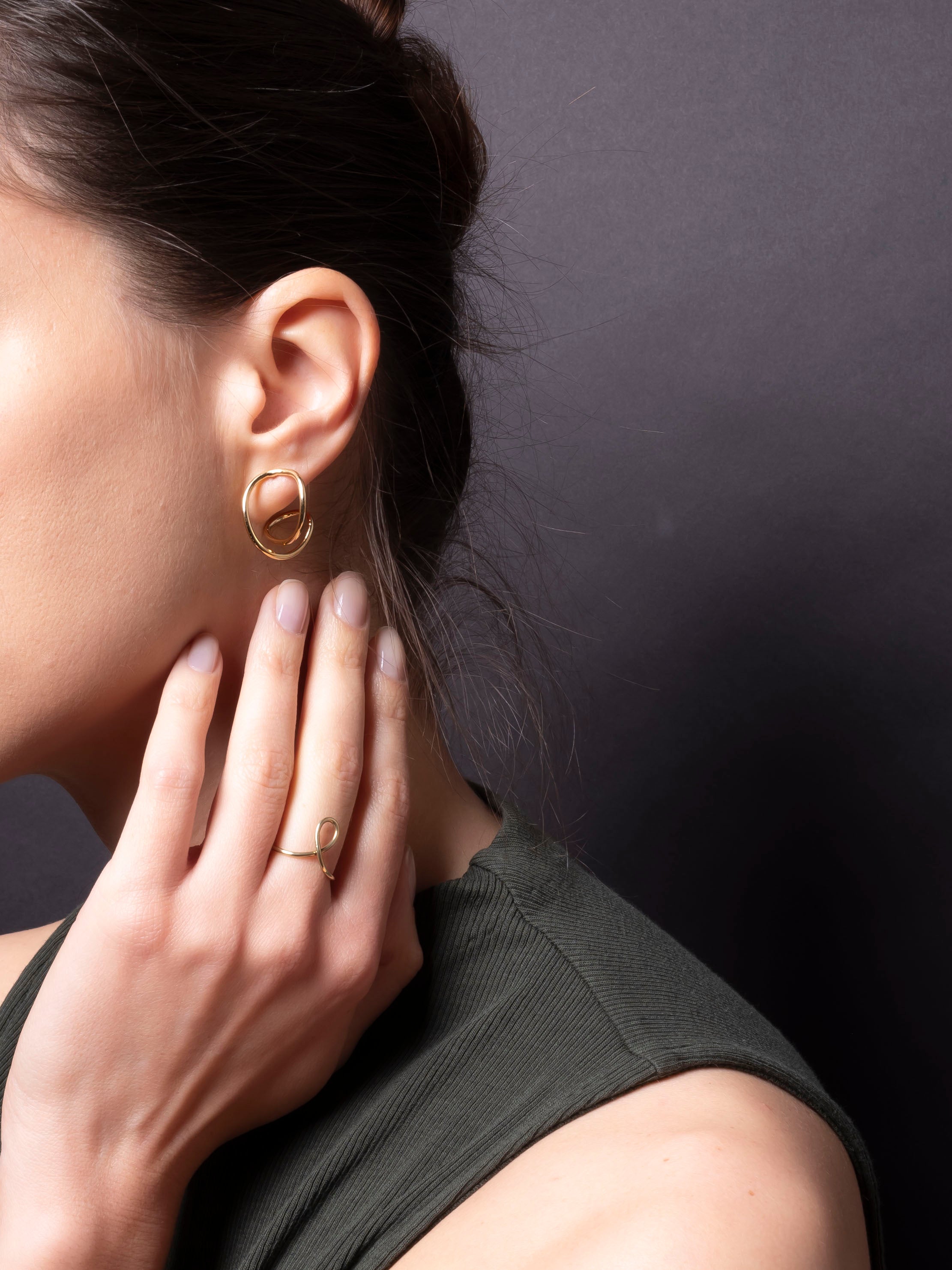 Close-up of a person wearing gold hoop earrings and a ring, with a dark background.