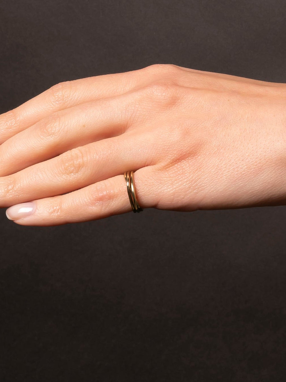 Hand wearing a gold ring on a dark background