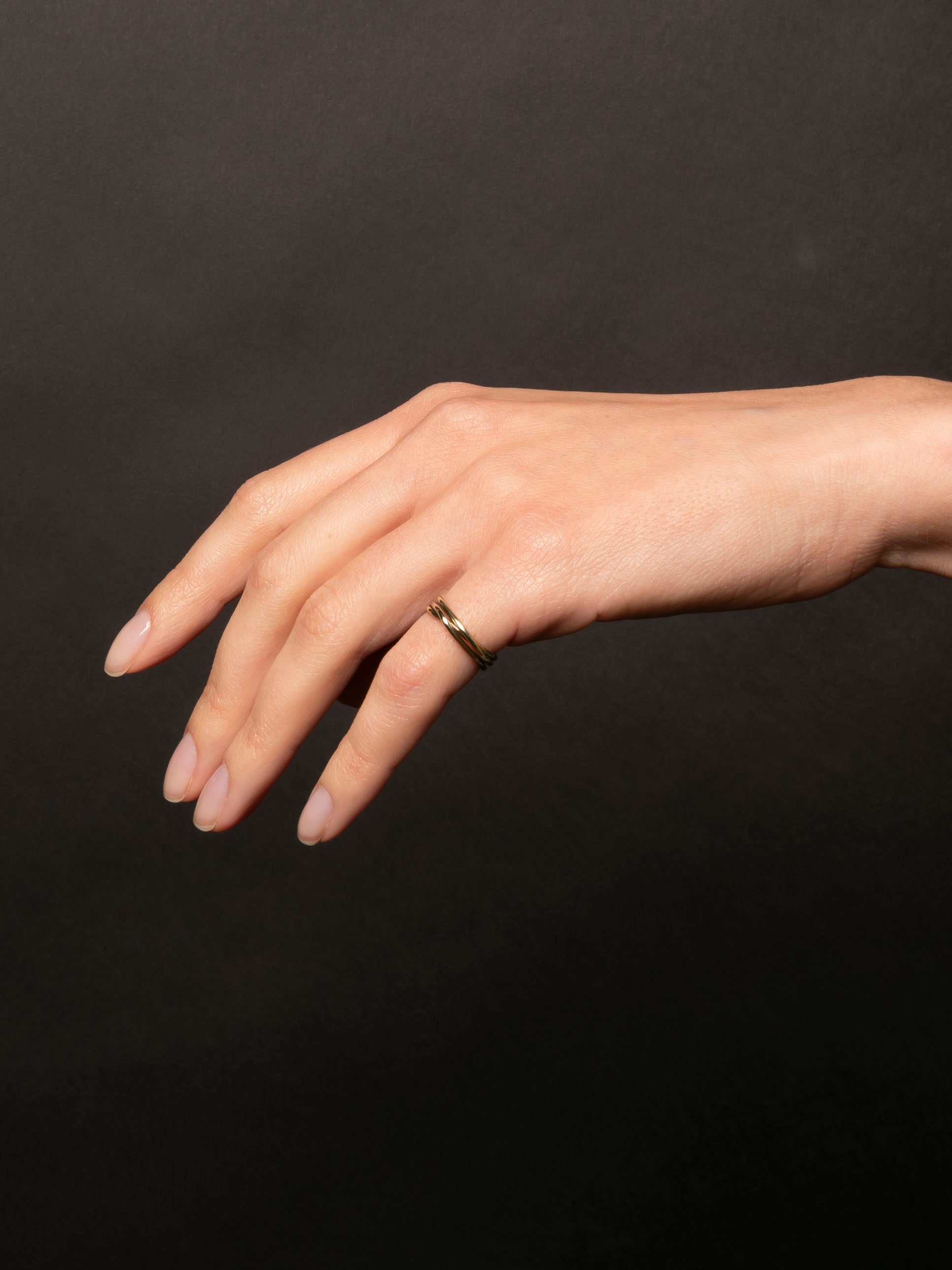 Hand wearing a gold ring on a dark background
