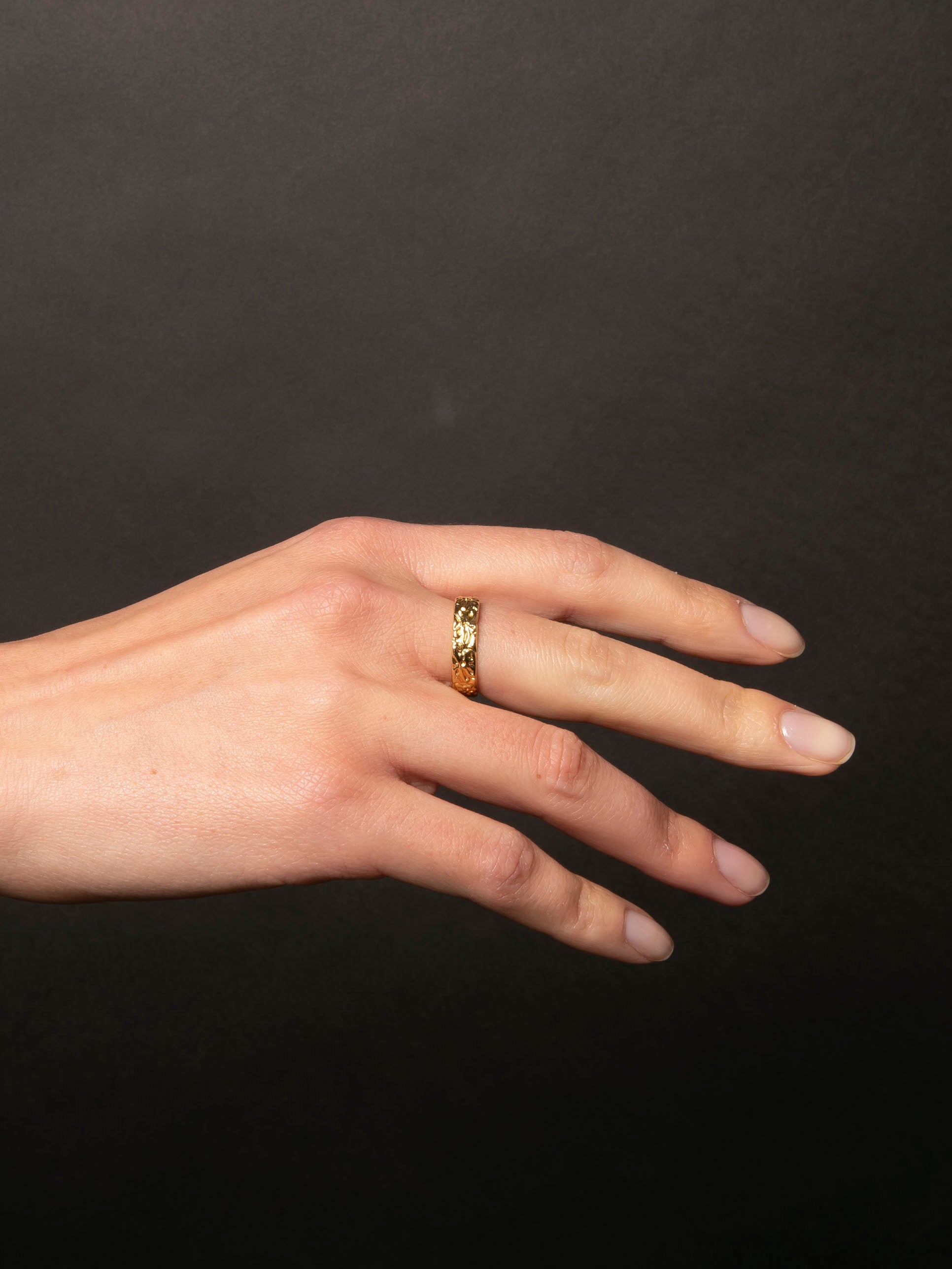 Hand wearing a gold ring on a black background