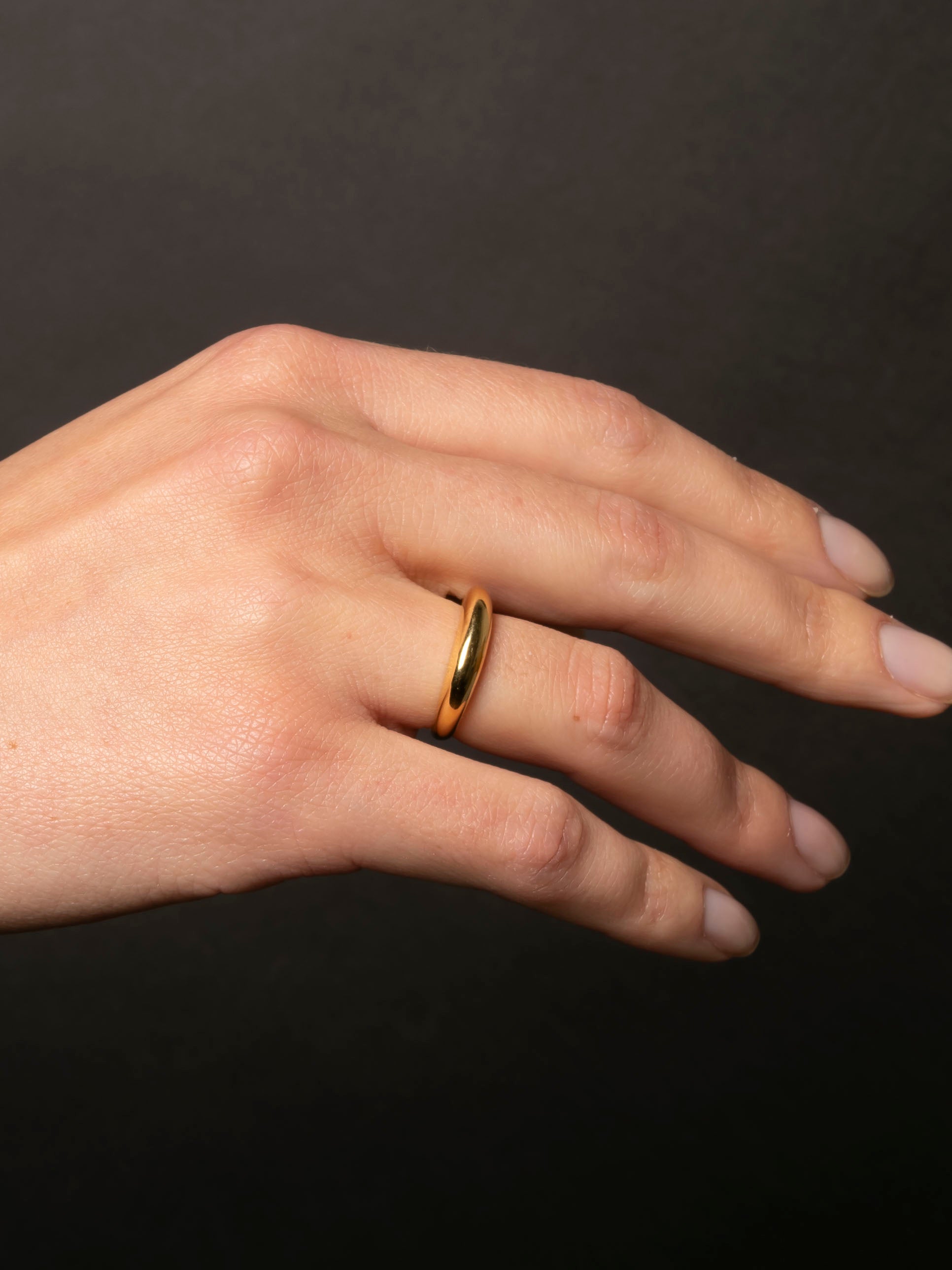 Hand wearing a gold ring on a dark background