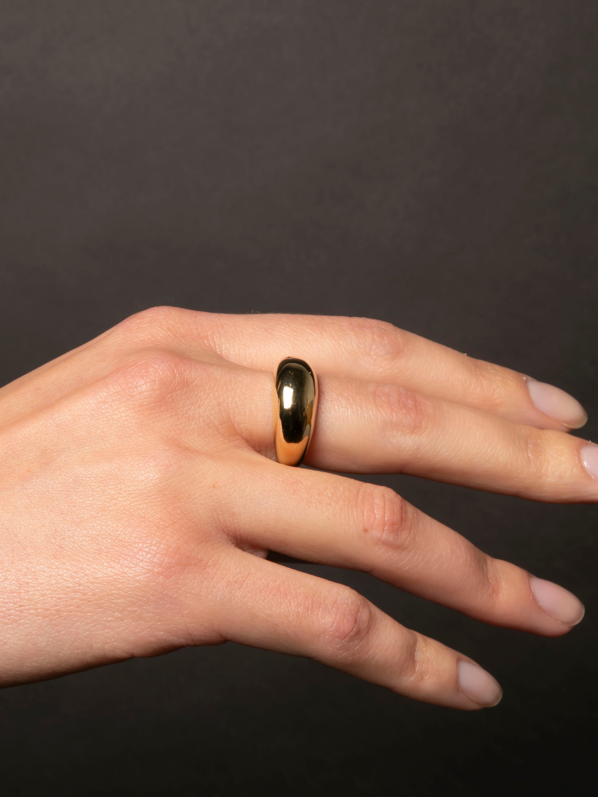 Gold ring on a person's finger against a dark background