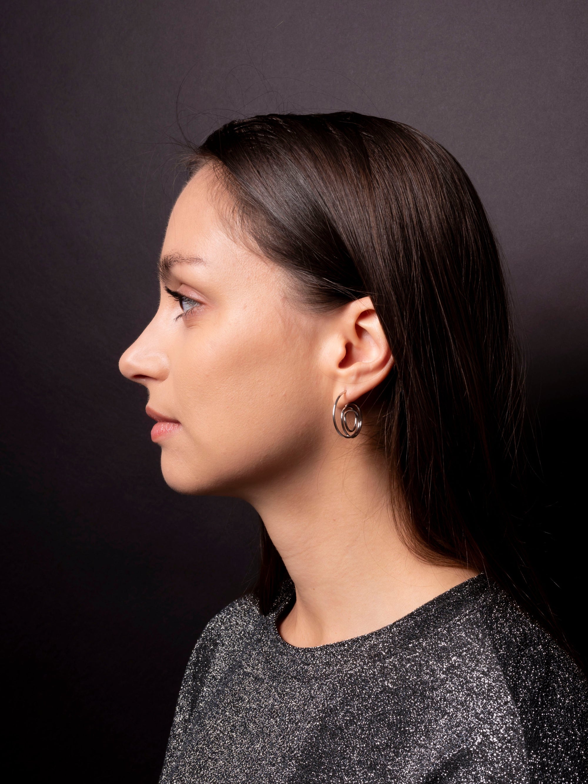 Side profile of a person with dark hair and earrings against a dark background