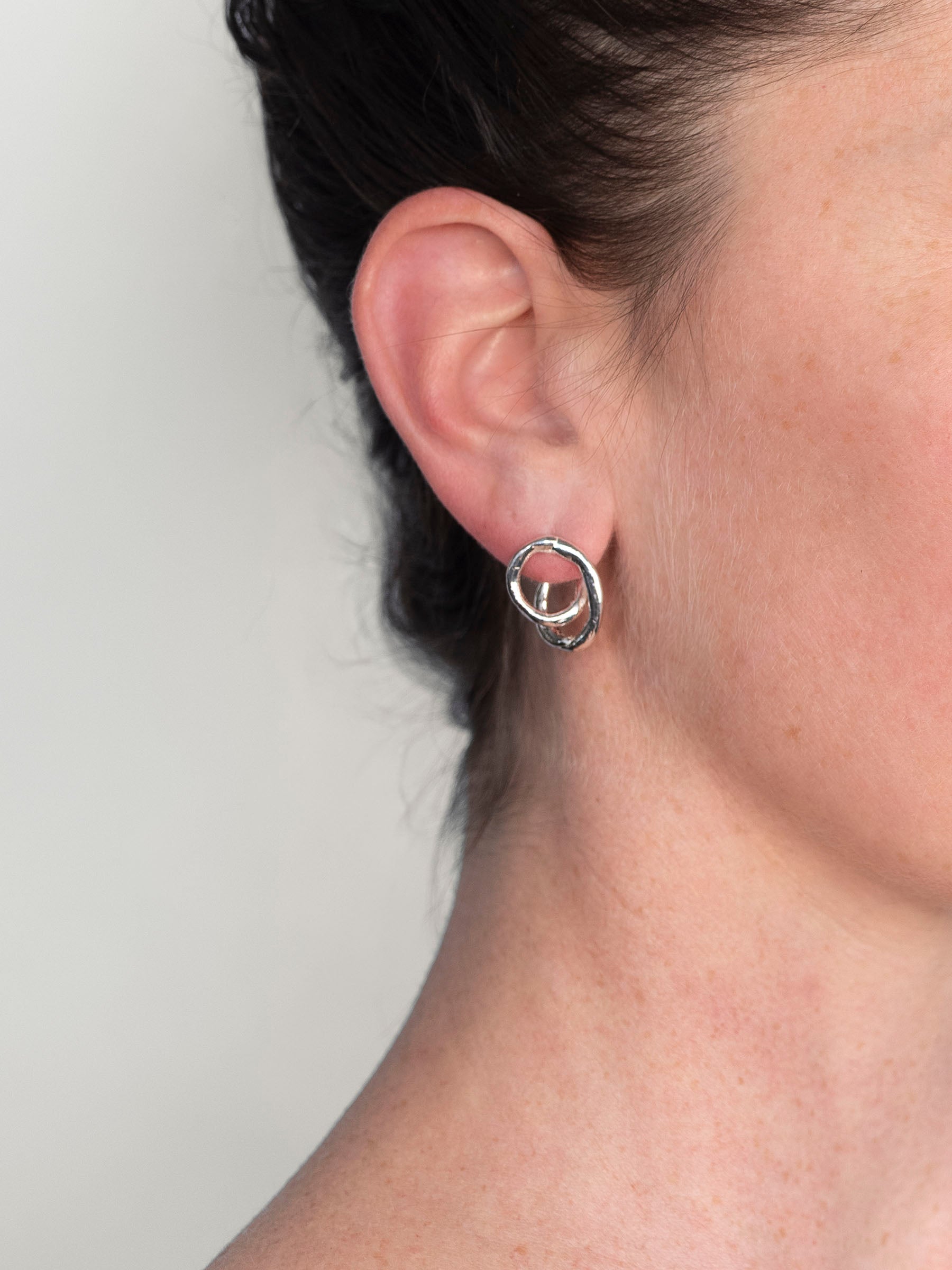 Close-up of an ear wearing a silver hoop earring against a neutral background