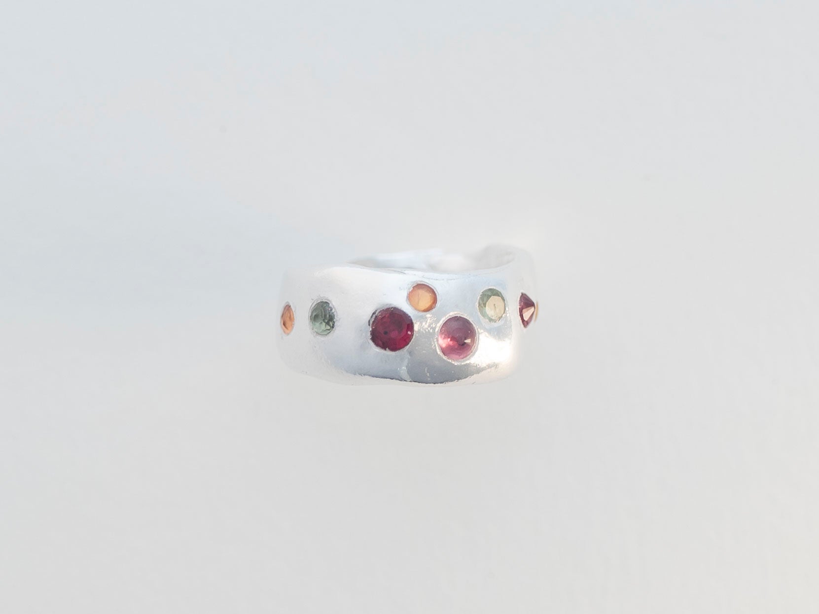 Silver ring with multicolored gemstones on a light gray background