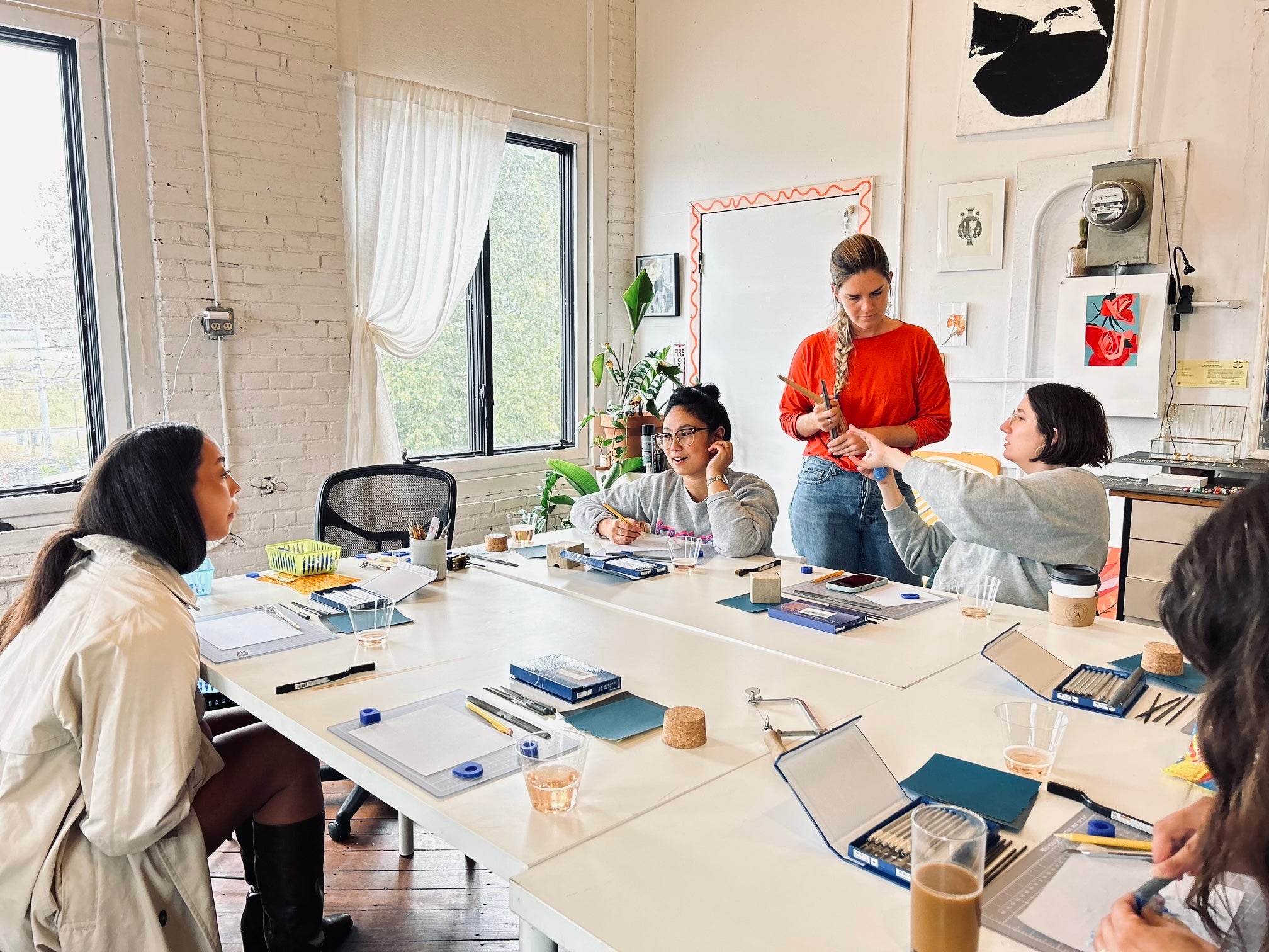 Group of people with jewelry making tools, wax and coffee cups on a table.