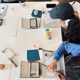 Two people working at a table with art supplies and snacks.