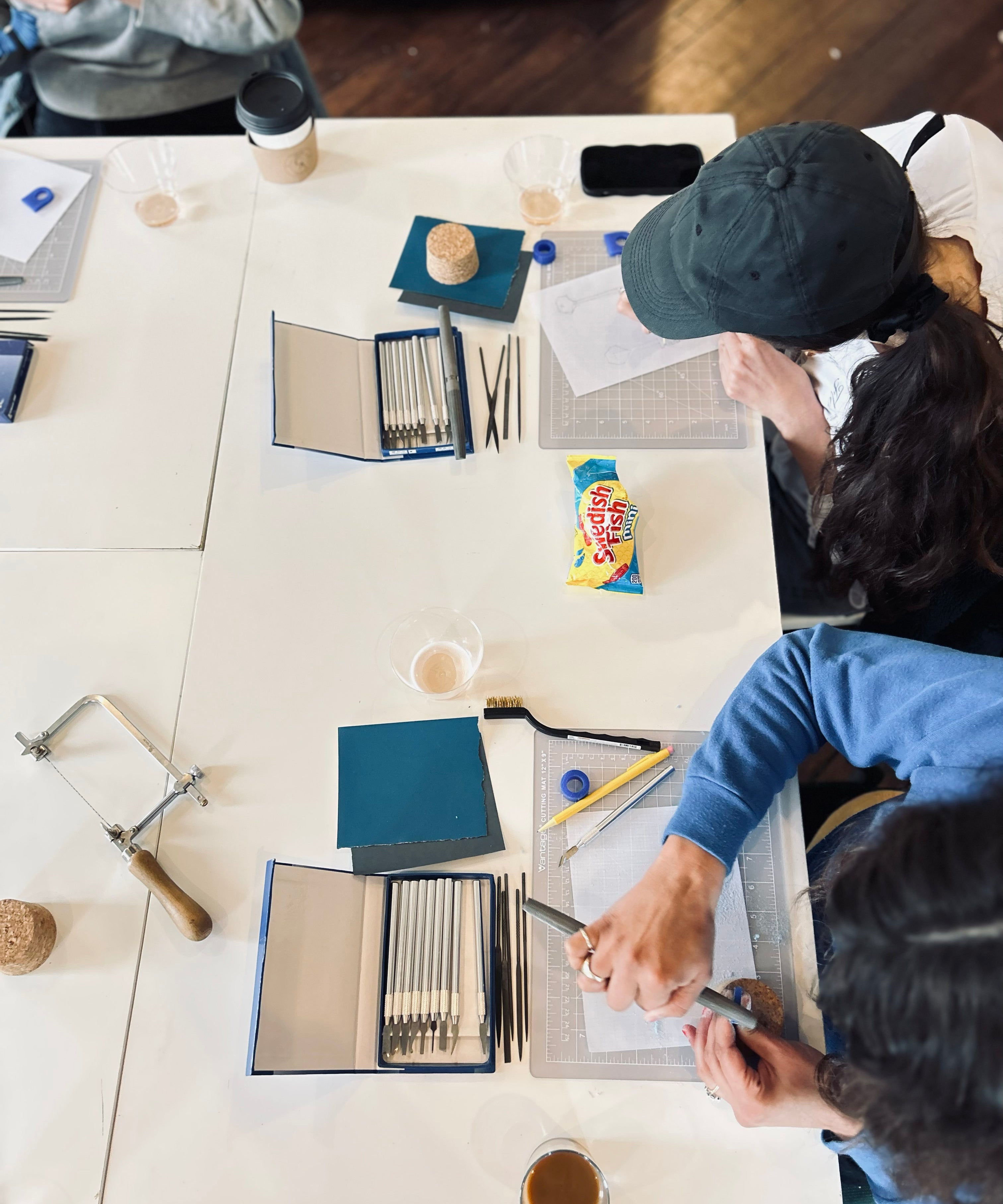 Two people working at a table with art supplies and snacks.