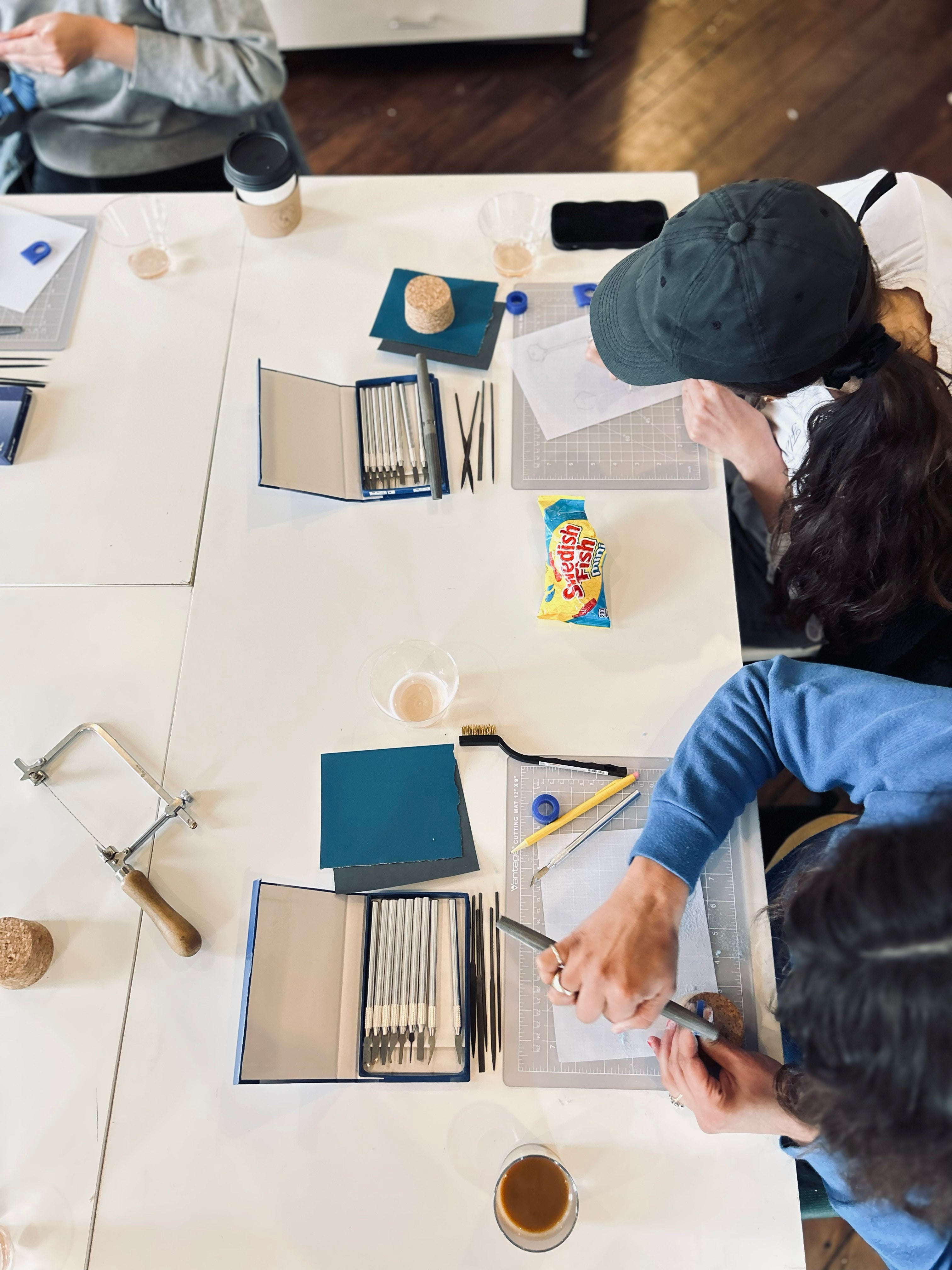 Two people working at a table with art supplies and snacks.