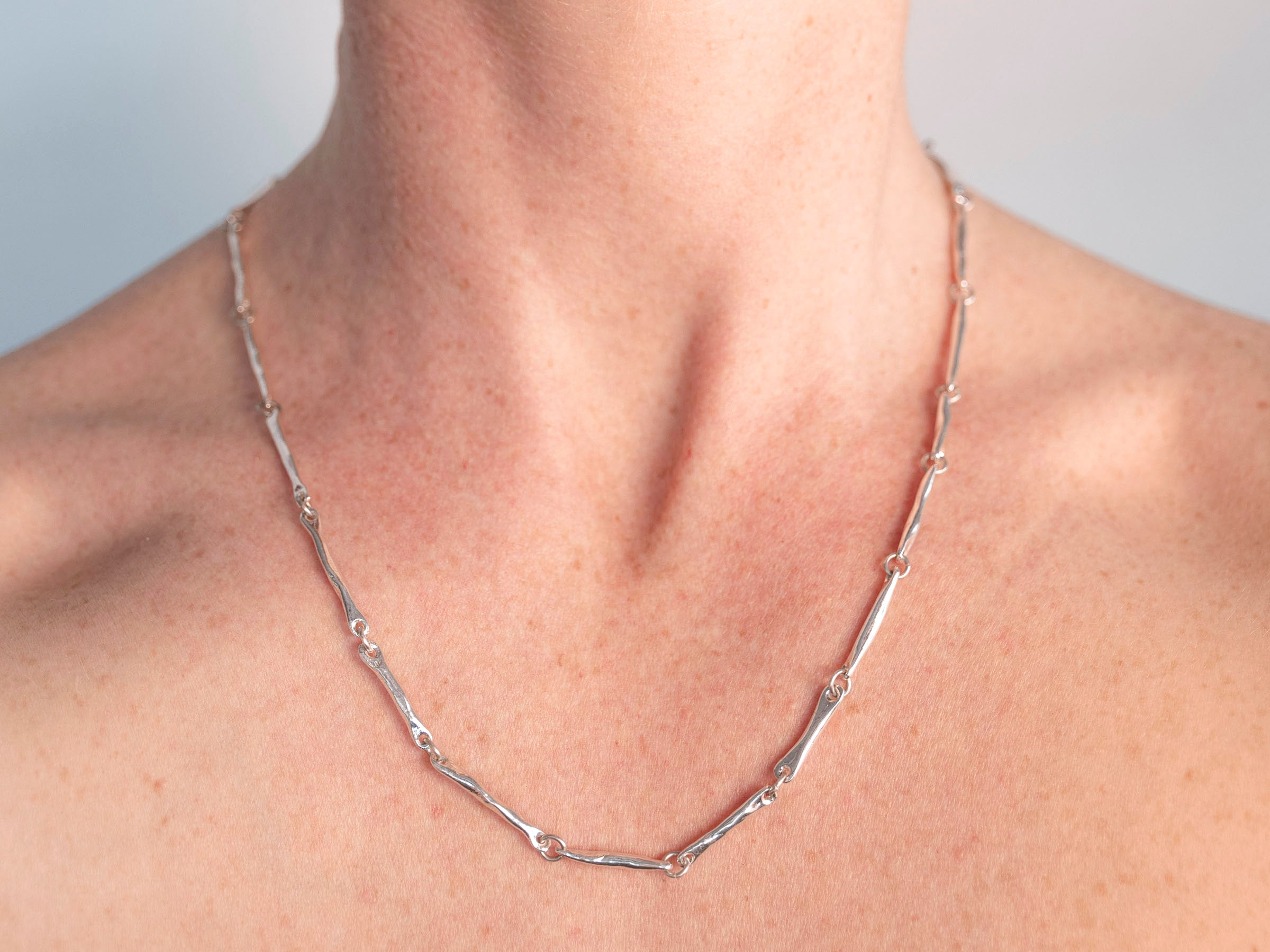 Silver necklace on a person's neck with a neutral background