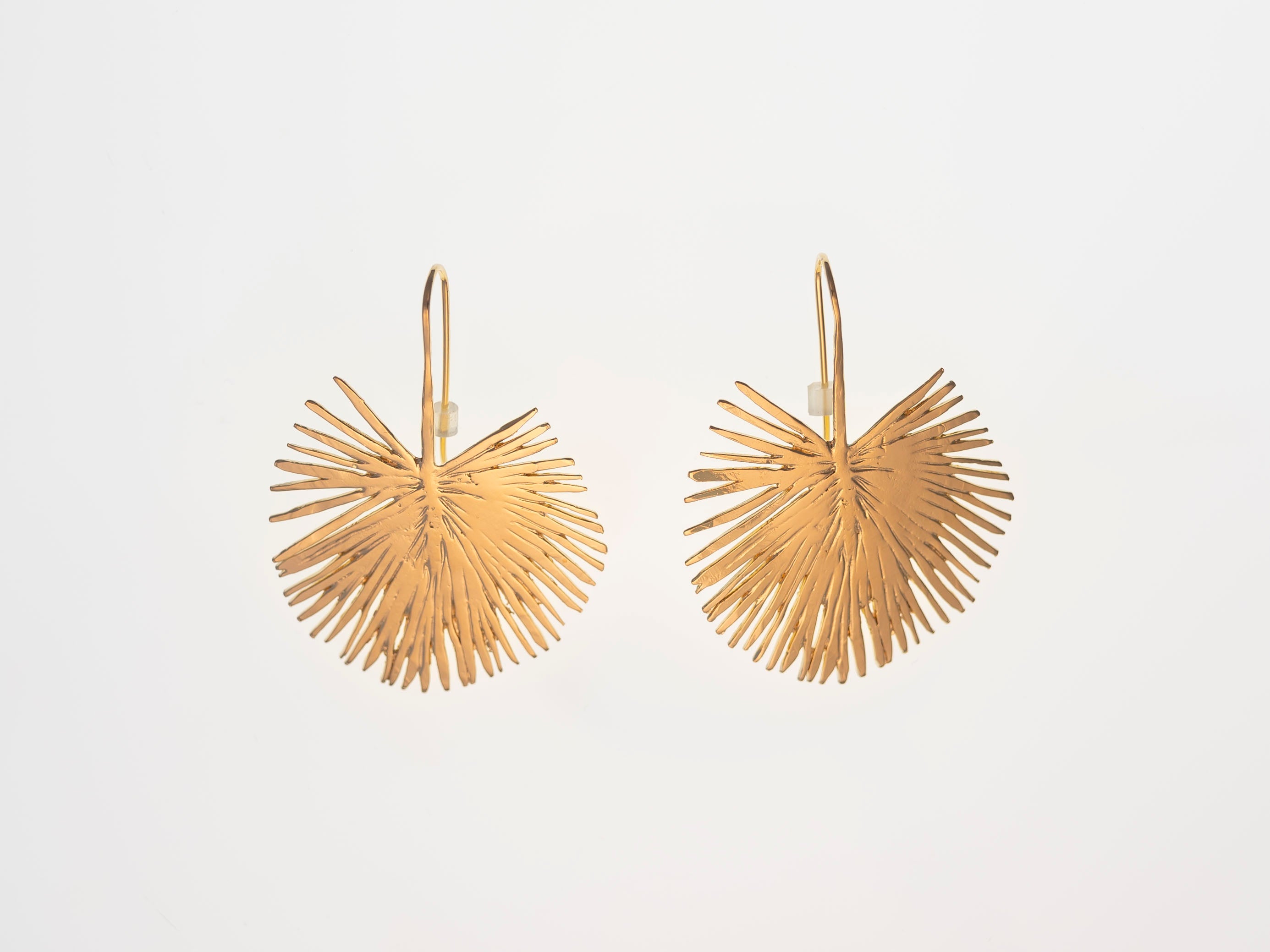 Gold earrings with a fan-like design on a light gray background