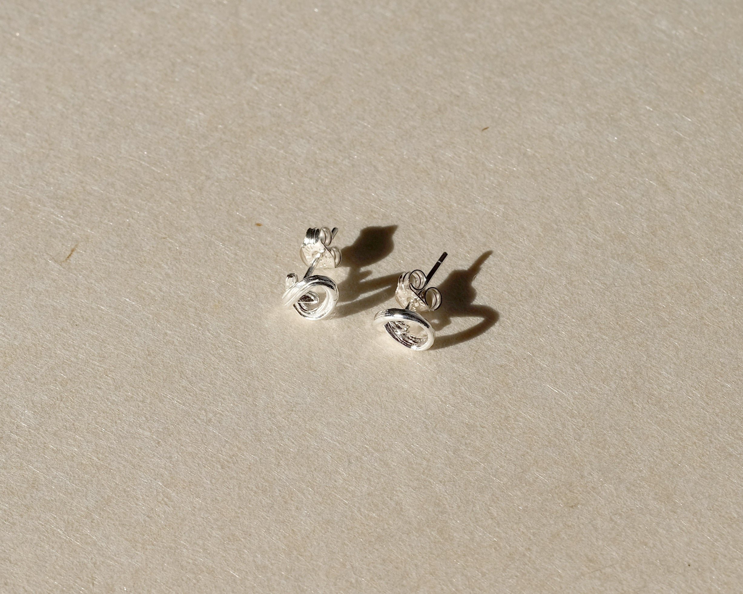 Sculptural sterling silver stud earrings with posts and butterfly backs on beige paper