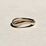 Curved sculptural 14k yellow gold wedding band on pale grey paper