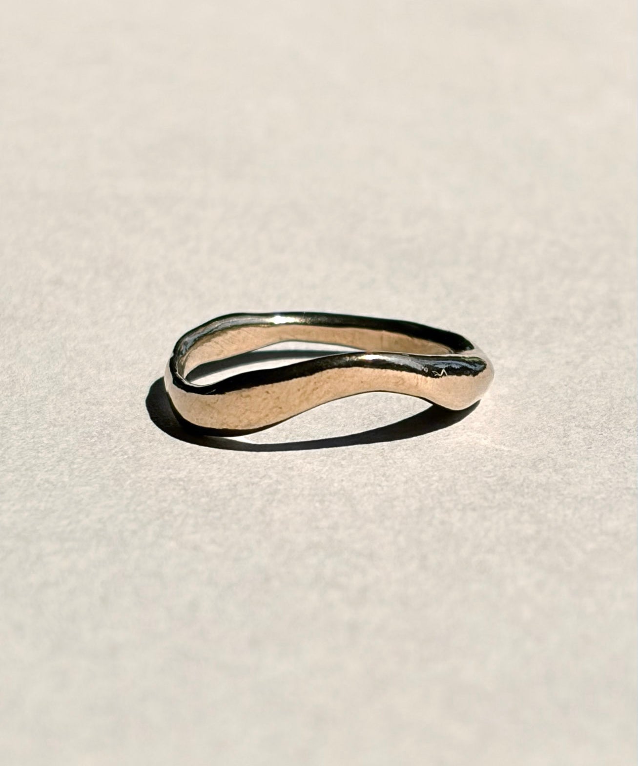 Curved sculptural 14k yellow gold wedding band on pale grey paper