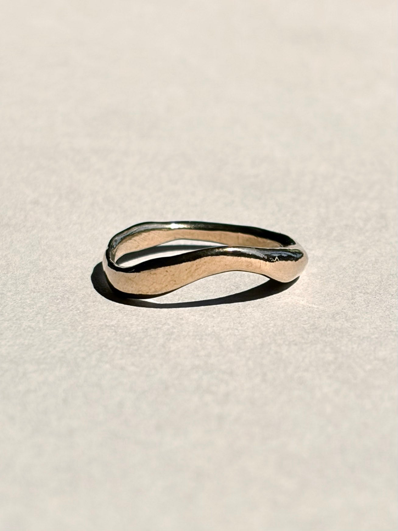 Curved sculptural 14k yellow gold wedding band on pale grey paper