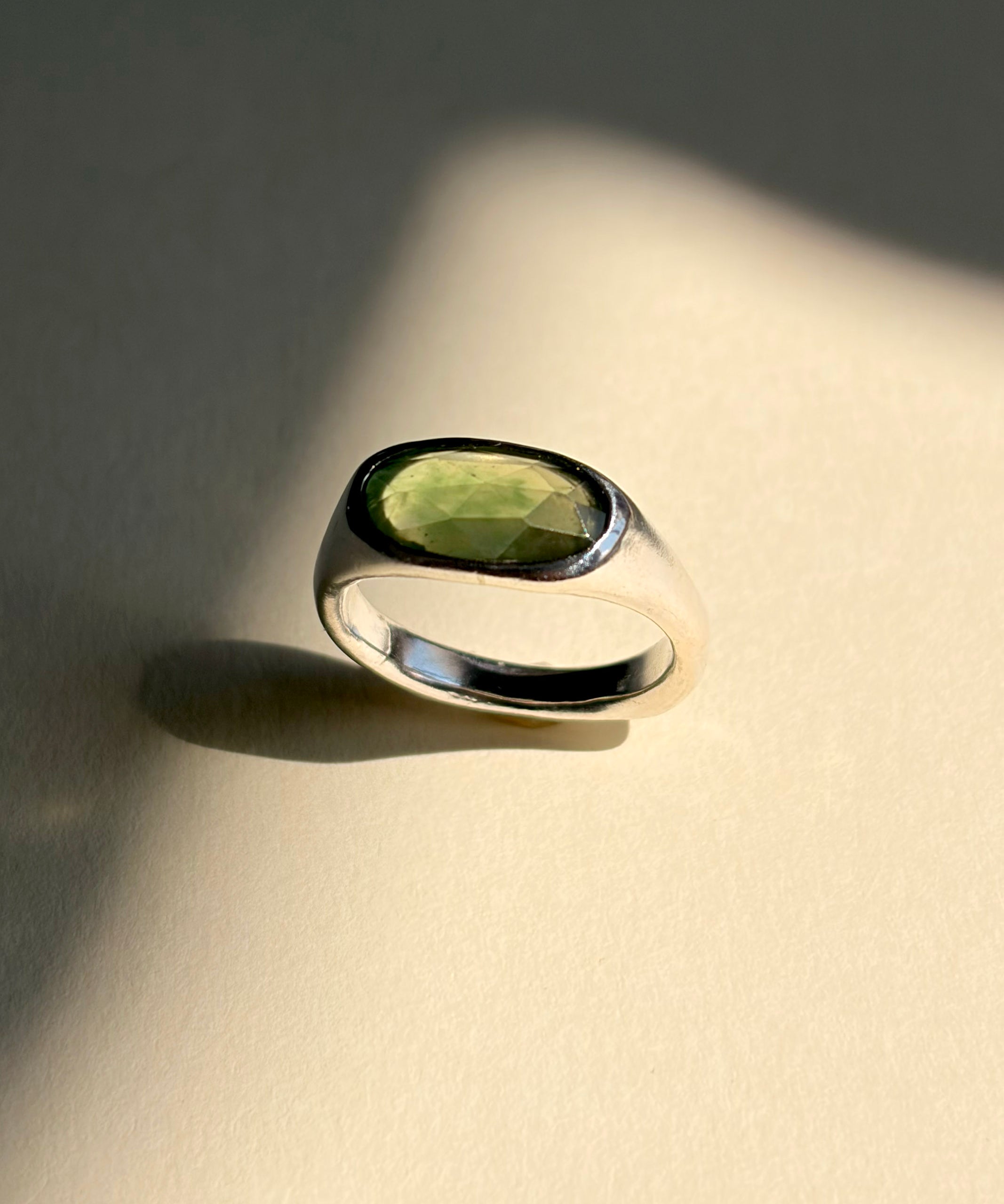 Green garnet set in a sculptural sterling silver ring, still life with shadows