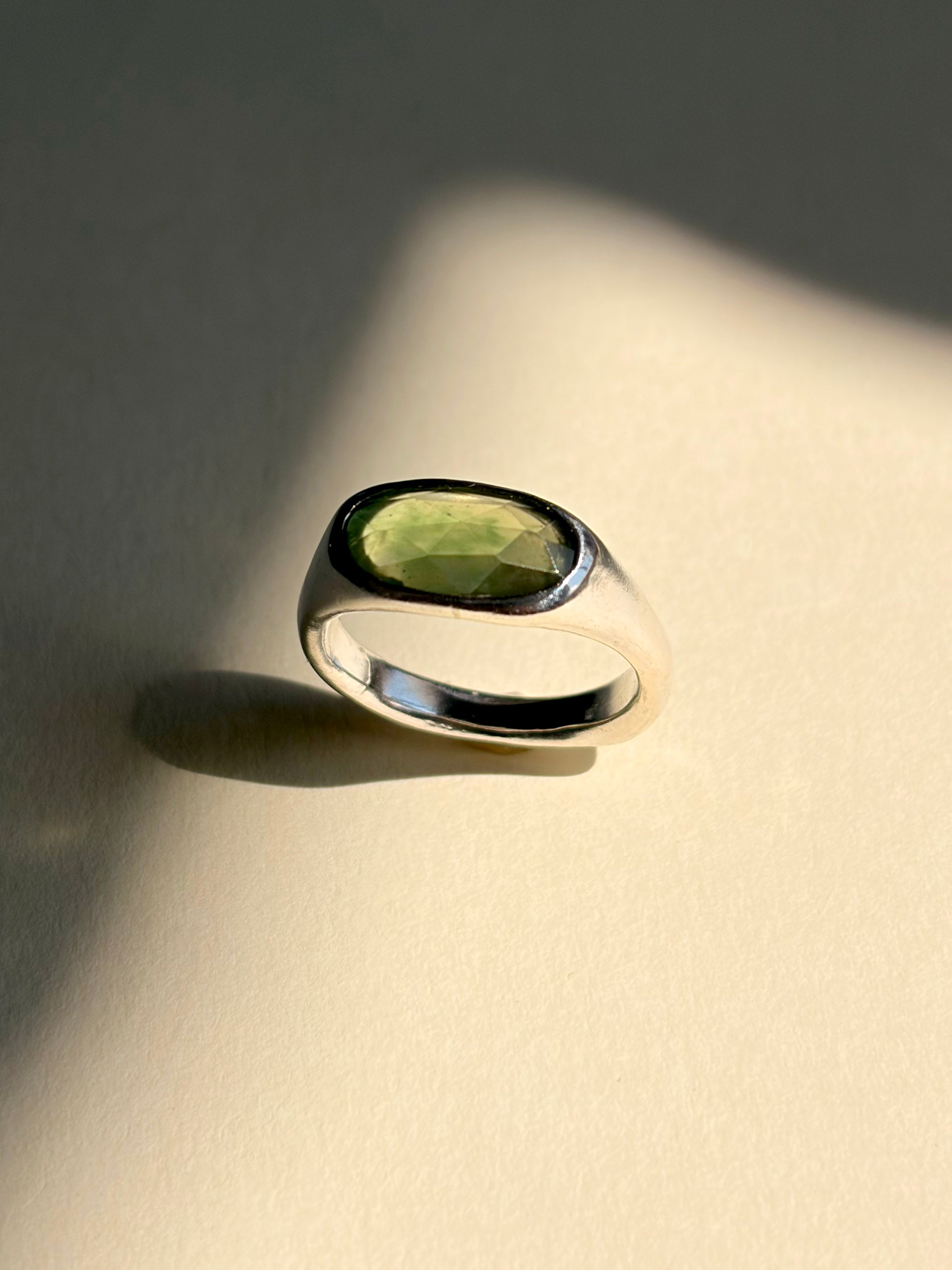 Green garnet set in a sculptural sterling silver ring, still life with shadows