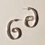 Pair of large sterling silver spiral earrings on beige paper