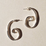 Pair of large sterling silver spiral earrings on beige paper
