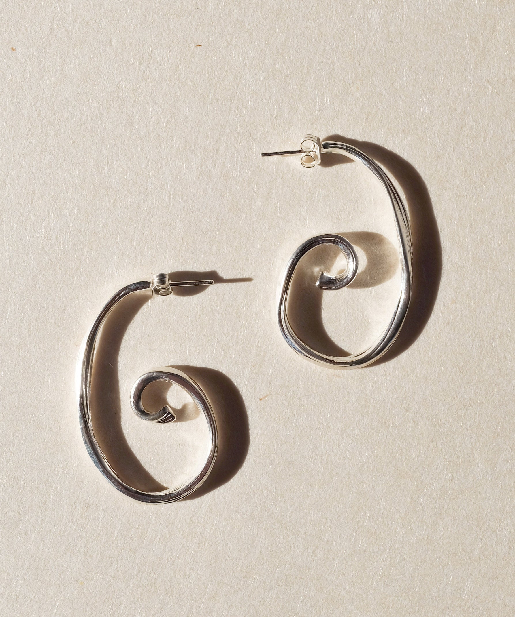 Pair of large sterling silver spiral earrings on beige paper