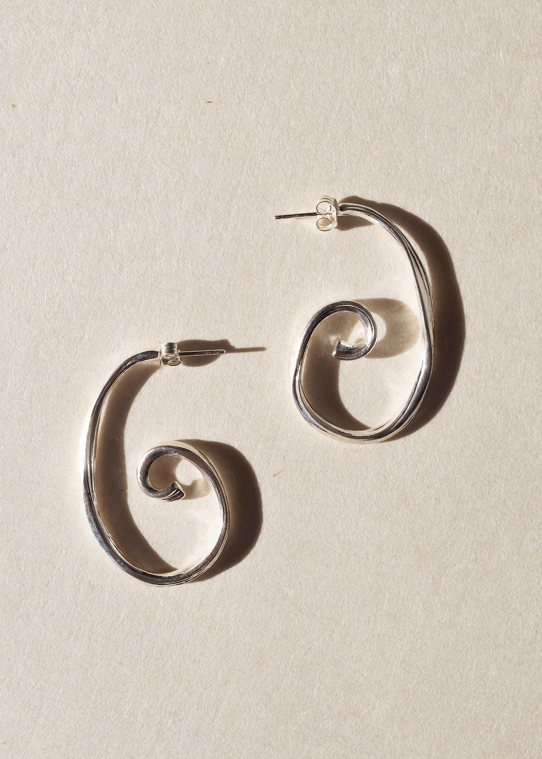 Pair of large sterling silver spiral earrings on beige paper
