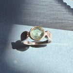 Pale green prehnite in a sculptural sterling silver ring on blue paper