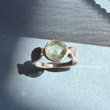 Pale green prehnite in a sculptural sterling silver ring on blue paper