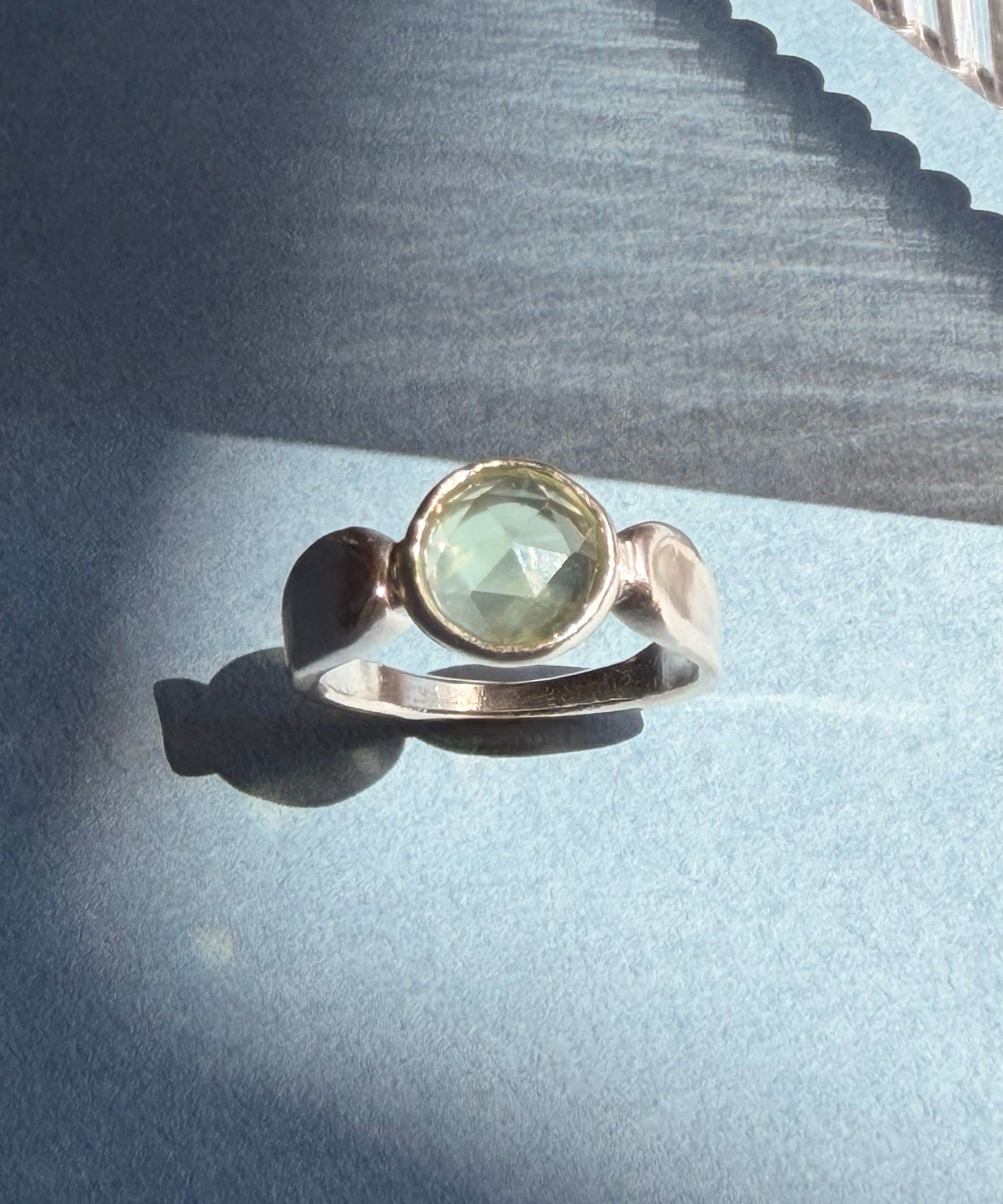 Pale green prehnite in a sculptural sterling silver ring on blue paper